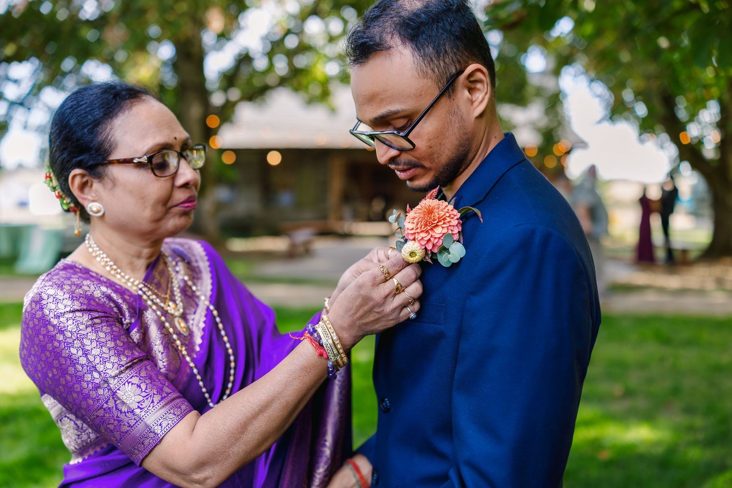 A couple in blue and purple attire share an intimate moment outdoors in a garden setting.