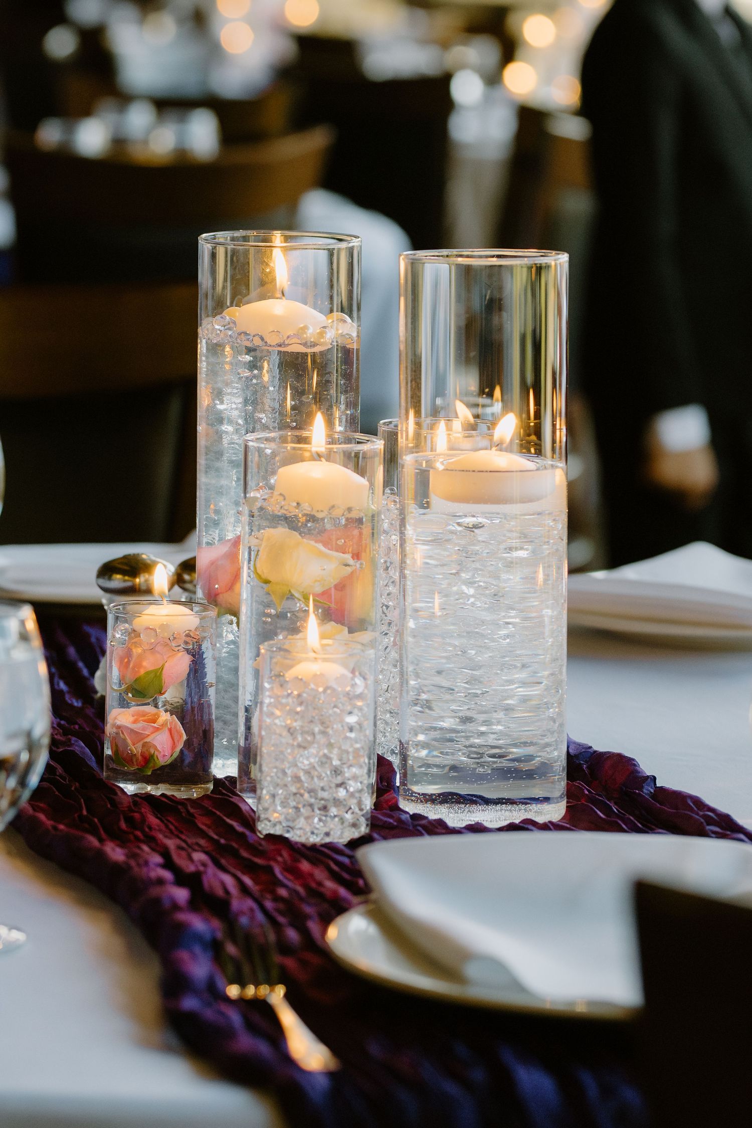 Elegant wedding reception table centerpiece with floating candles in tall glass cylinders and roses.