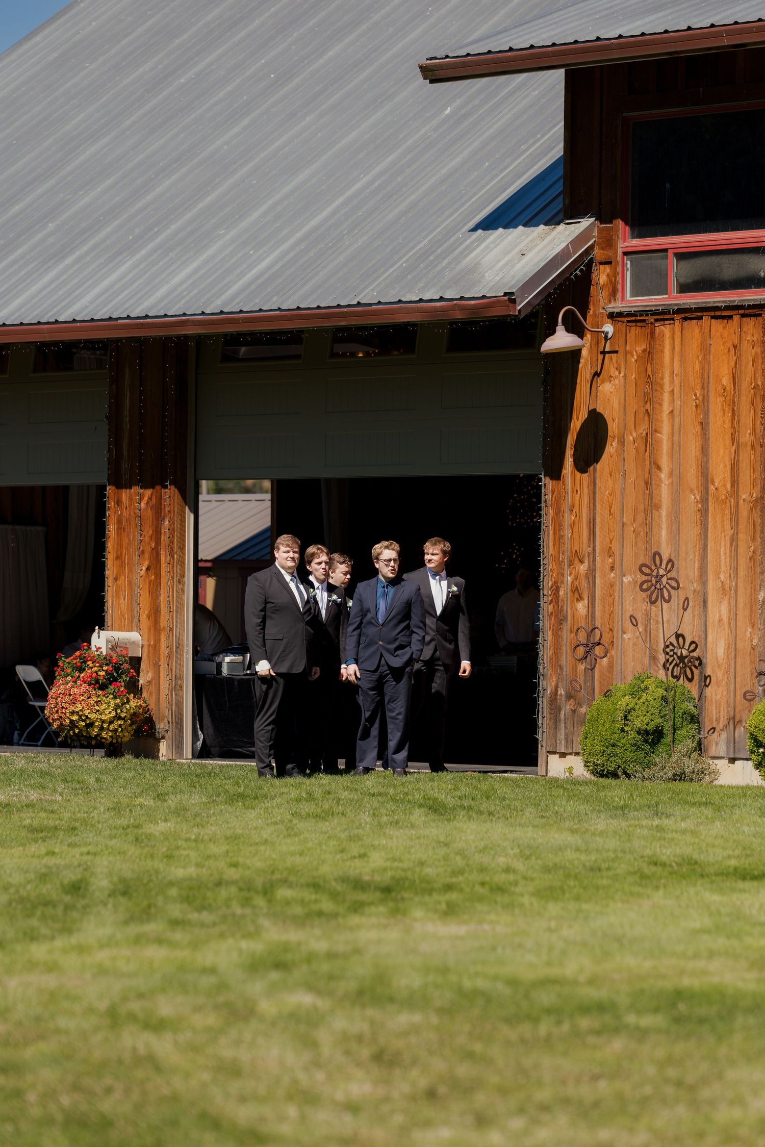 Group of groomsmen in dark suits standing in the entrance of a rustic wooden barn wedding venue.