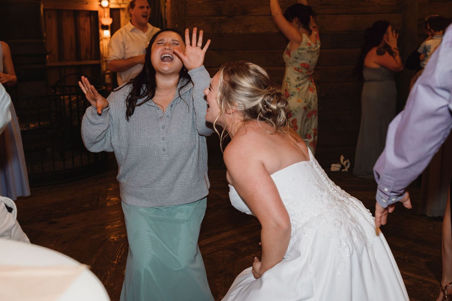 Bride in white gown dancing energetically with laughing guest at fun wedding reception celebration.