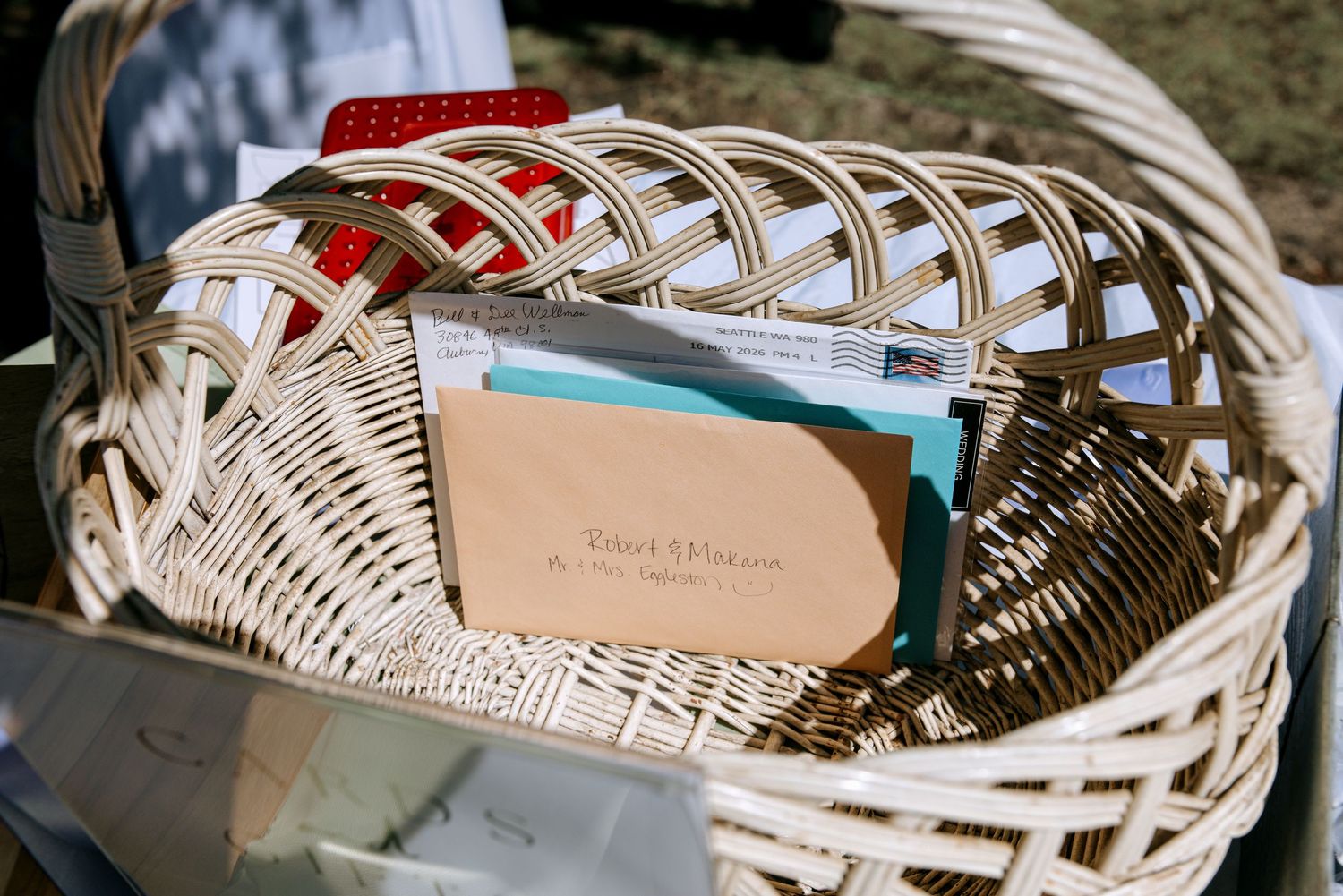 White wicker basket filled with wedding cards and envelopes at an outdoor wedding reception.