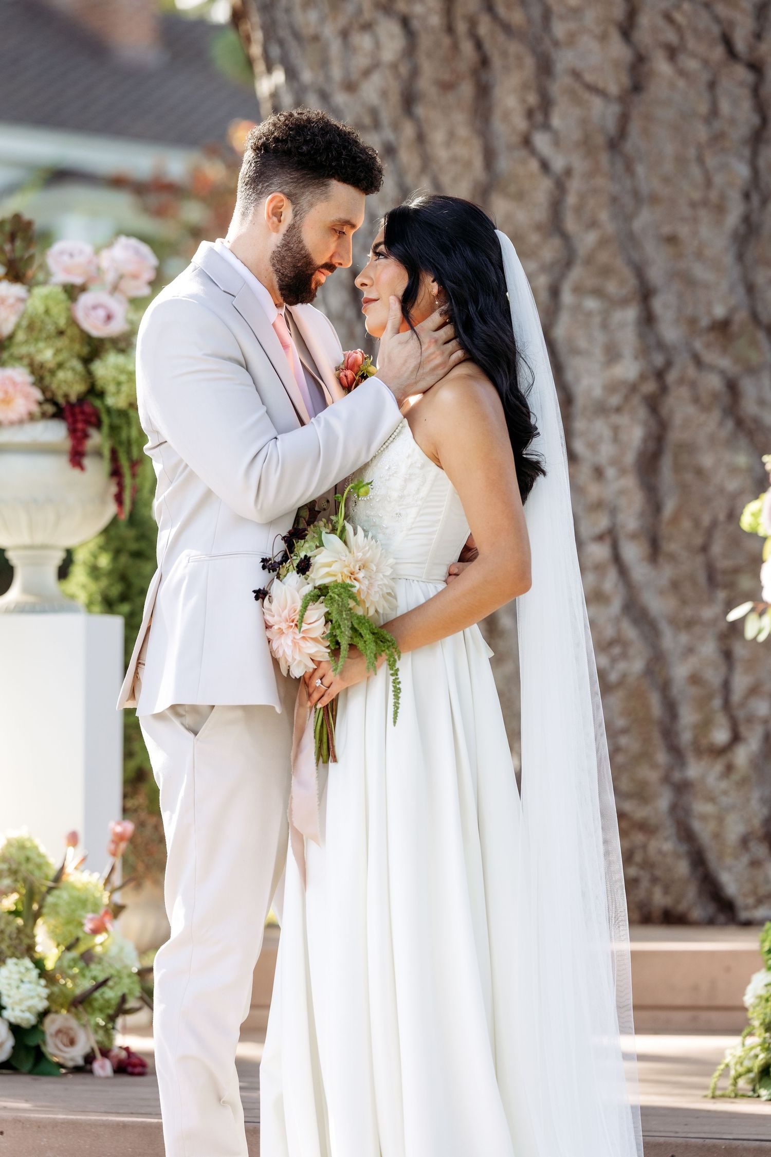 A romantic wedding couple shares intimate moments in a series of elegant outdoor portraits with floral decor.