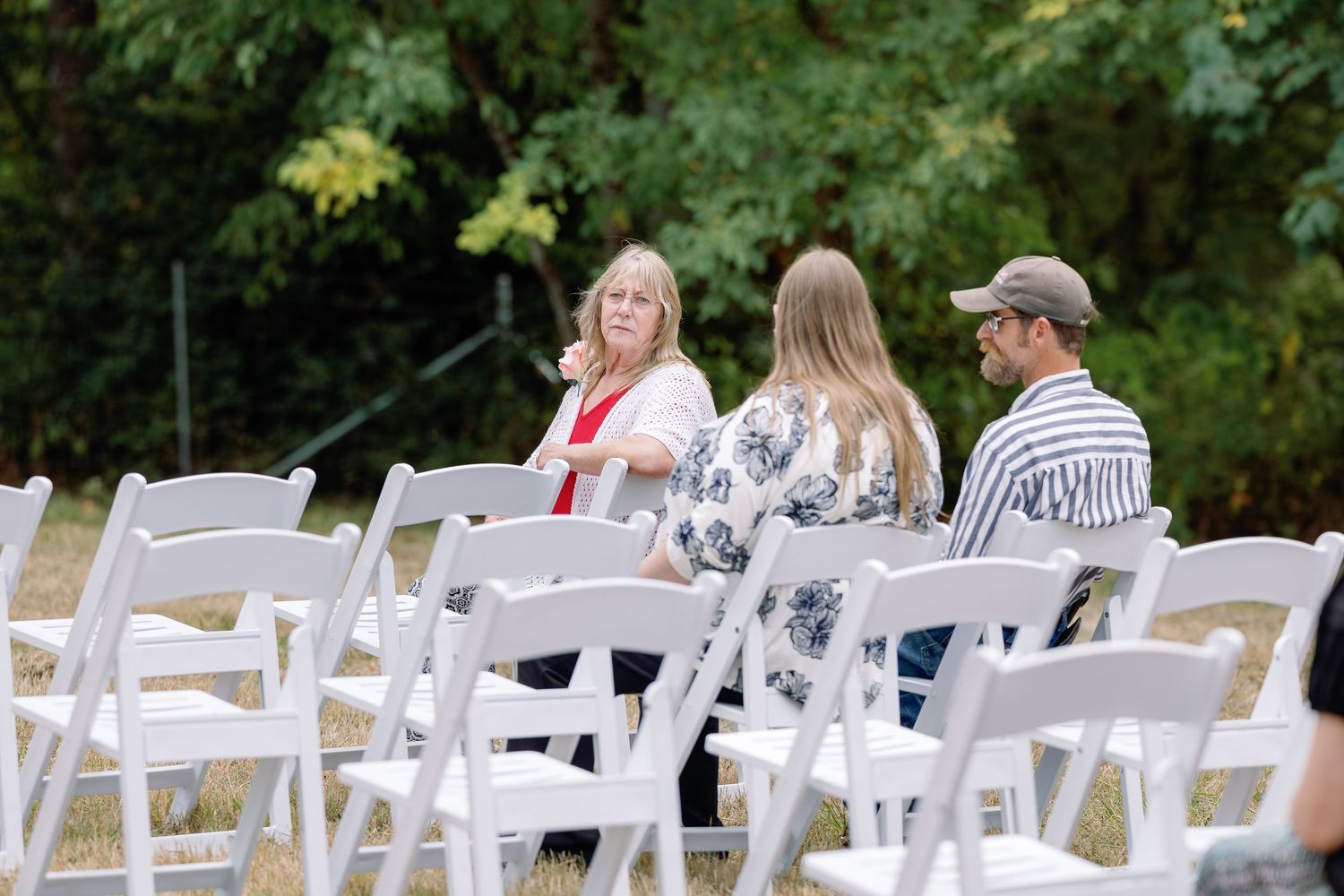 White folding chairs arranged in rows for an outdoor wedding ceremony with green trees in the background.