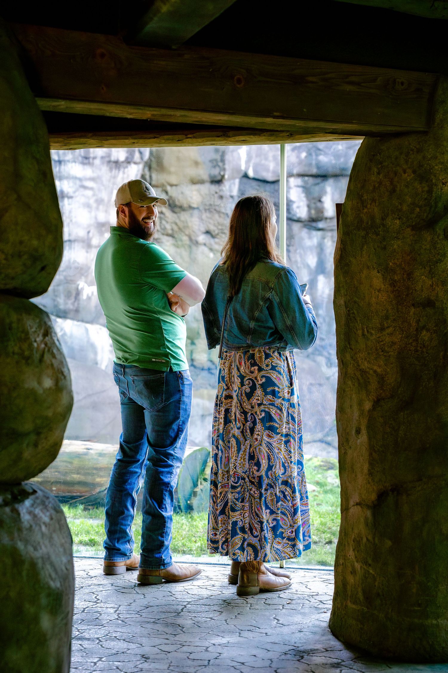 Two visitors stand in a stone archway viewing an outdoor exhibit at a zoo.