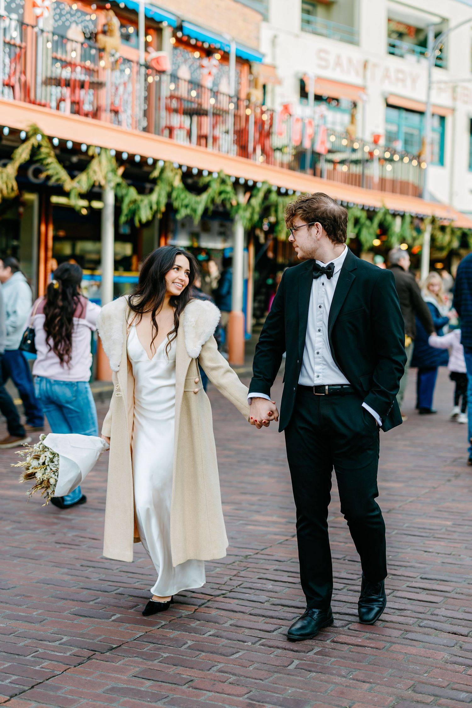 Couple in formal attire walking along brick sidewalk outside Pike Place Market in Seattle.
