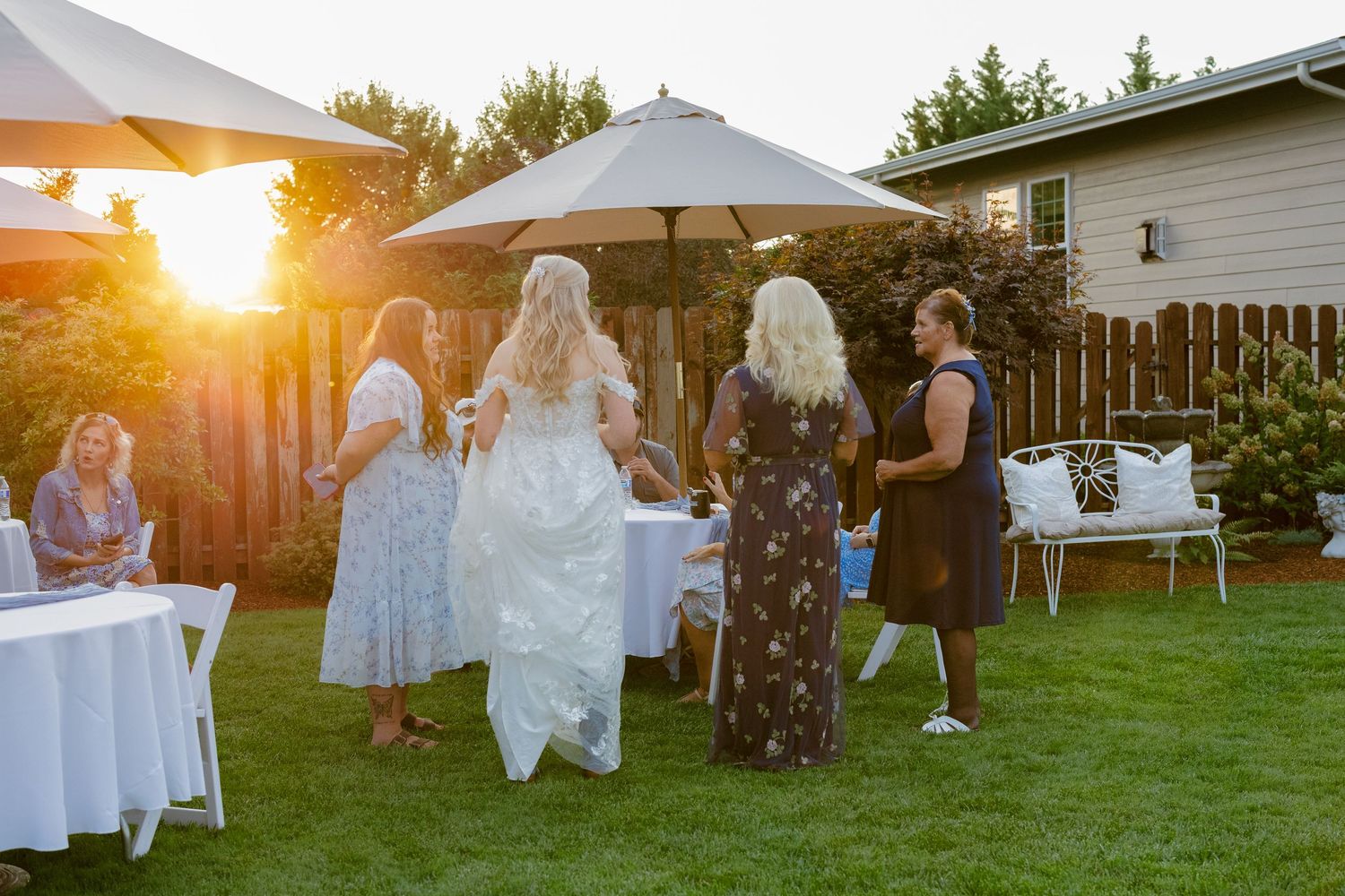 Guests seated in white chairs on a lawn at sunset during an outdoor wedding ceremony.