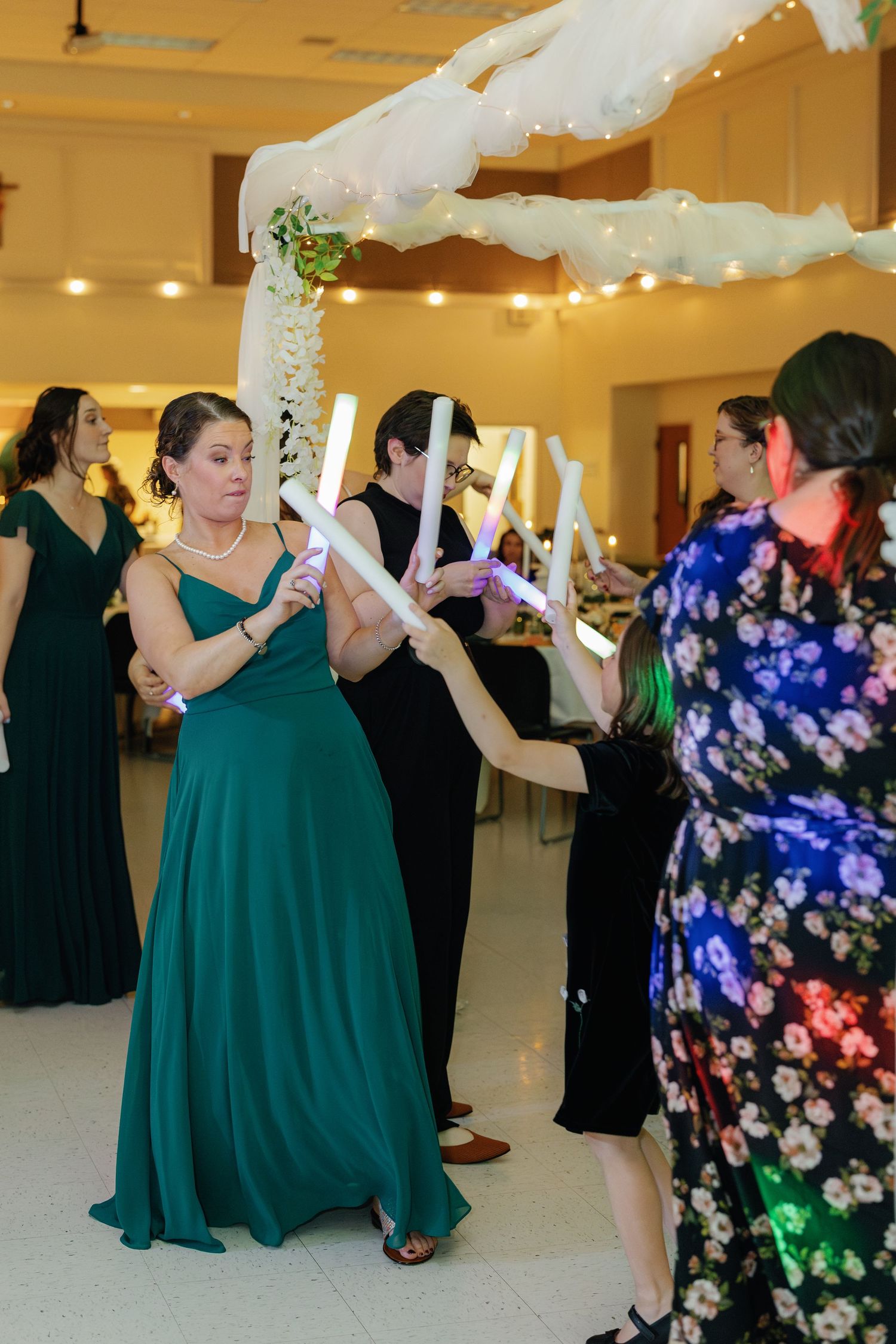 Wedding reception guests dance together in a banquet hall with emerald green dresses and floral prints.