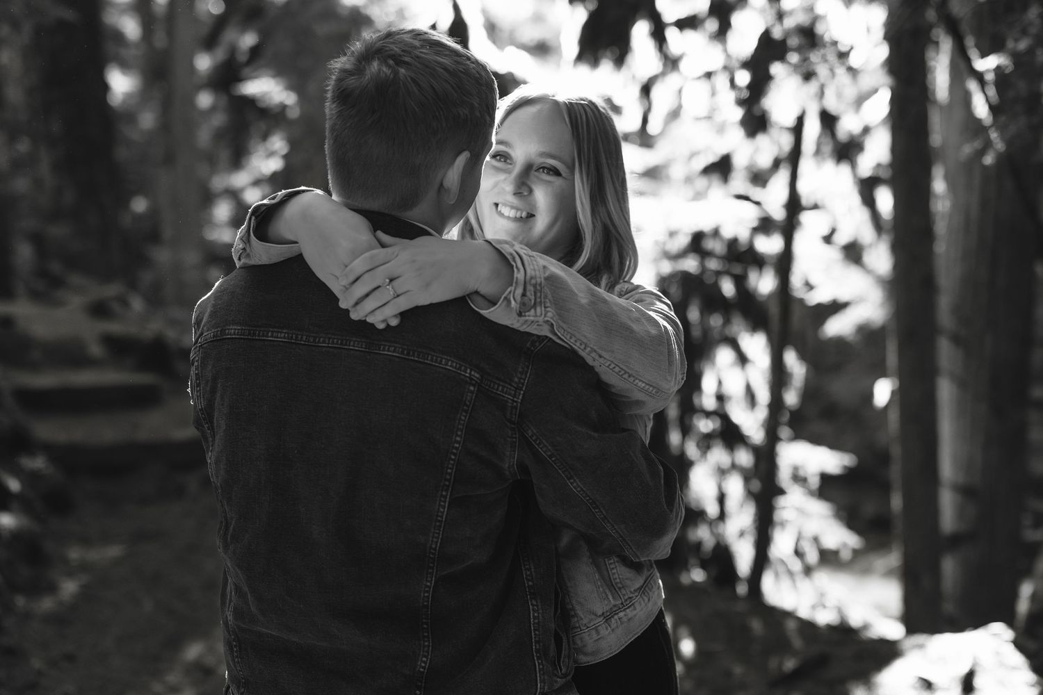A black and white photo of an intimate embrace in a wooded outdoor setting.