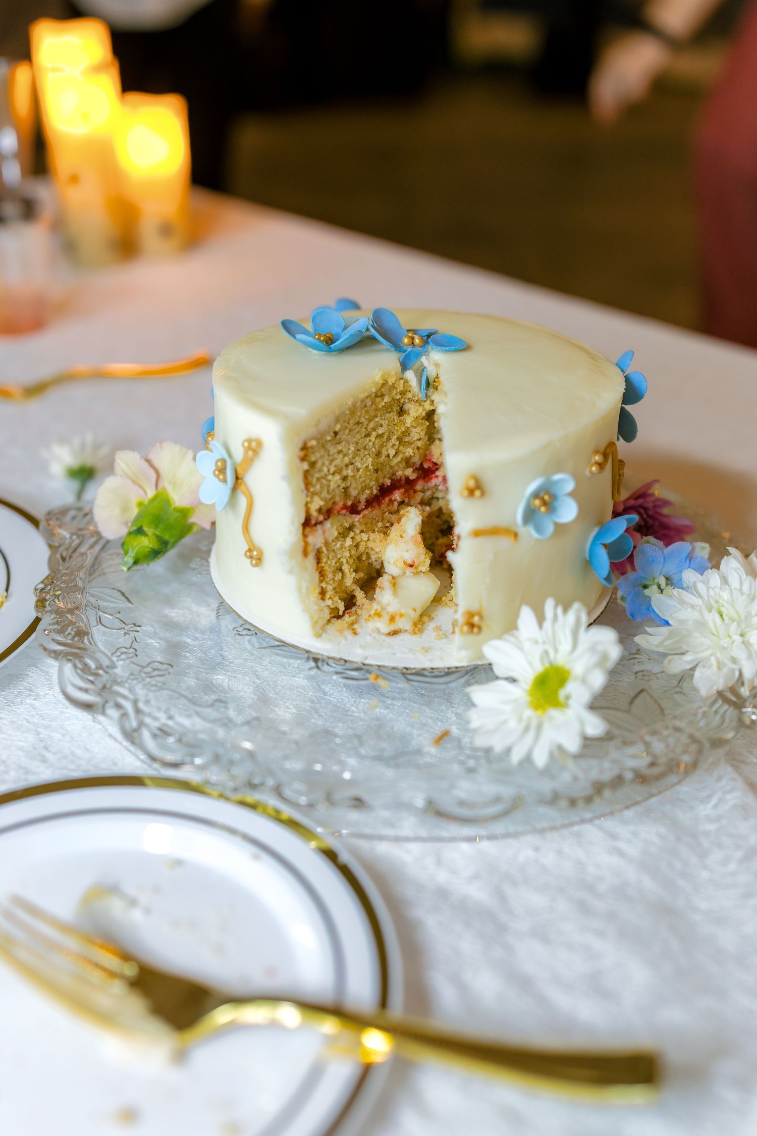 Slices of wedding cake decorated with delicate blue flowers and white daisies on ornate glass plates.