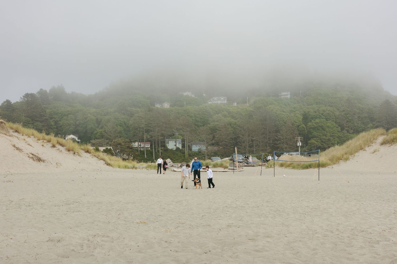 Misty coastal landscape with people walking along a foggy beach.
