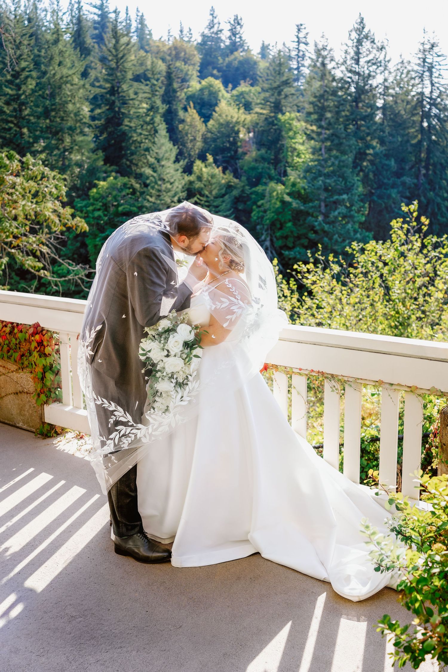 A romantic first look moment between newlyweds on a sunny outdoor porch surrounded by evergreen trees.