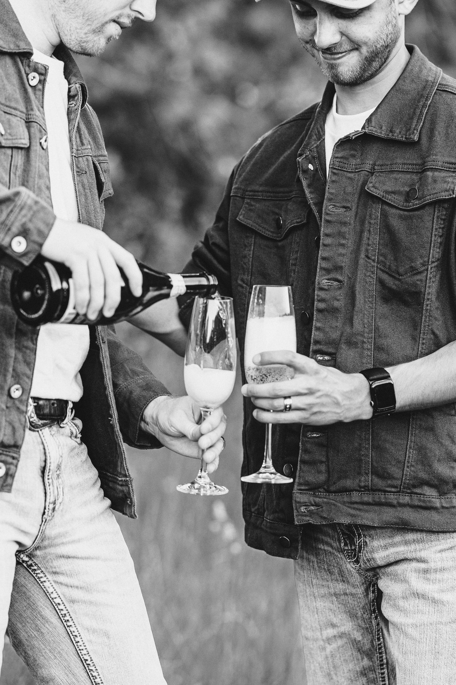 Close-up black and white photo of champagne being poured into flutes held by people wearing denim jackets.