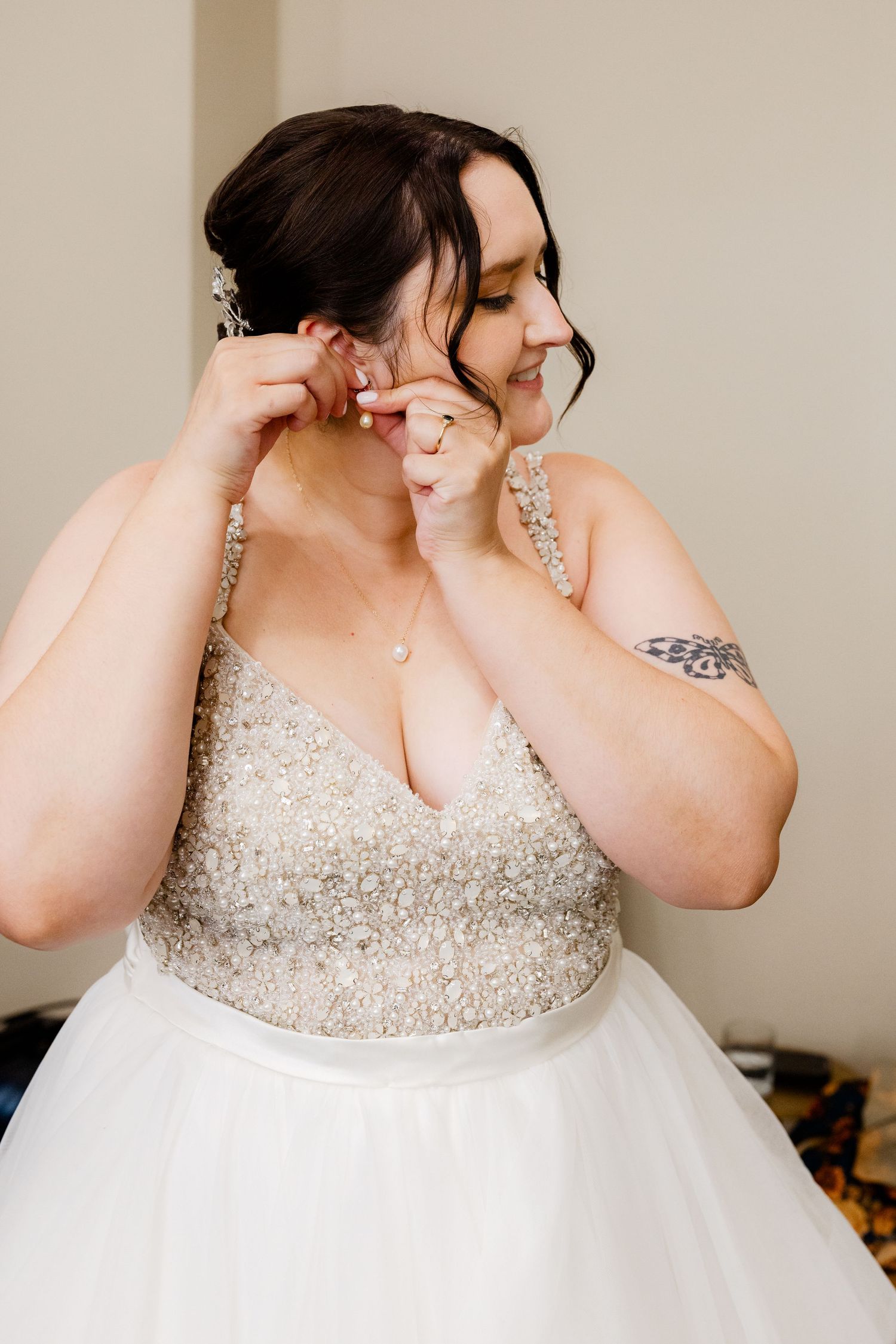 Bride in beaded wedding gown puts on earrings while smiling on her wedding day.