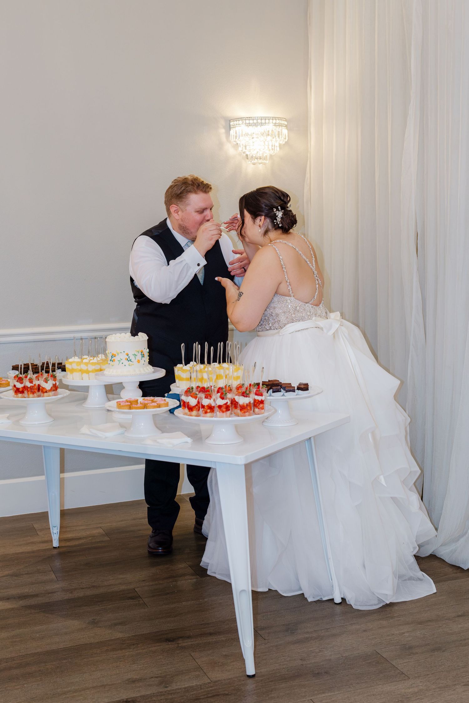 Bride and groom share a sweet cake tasting moment at their elegant wedding dessert table.