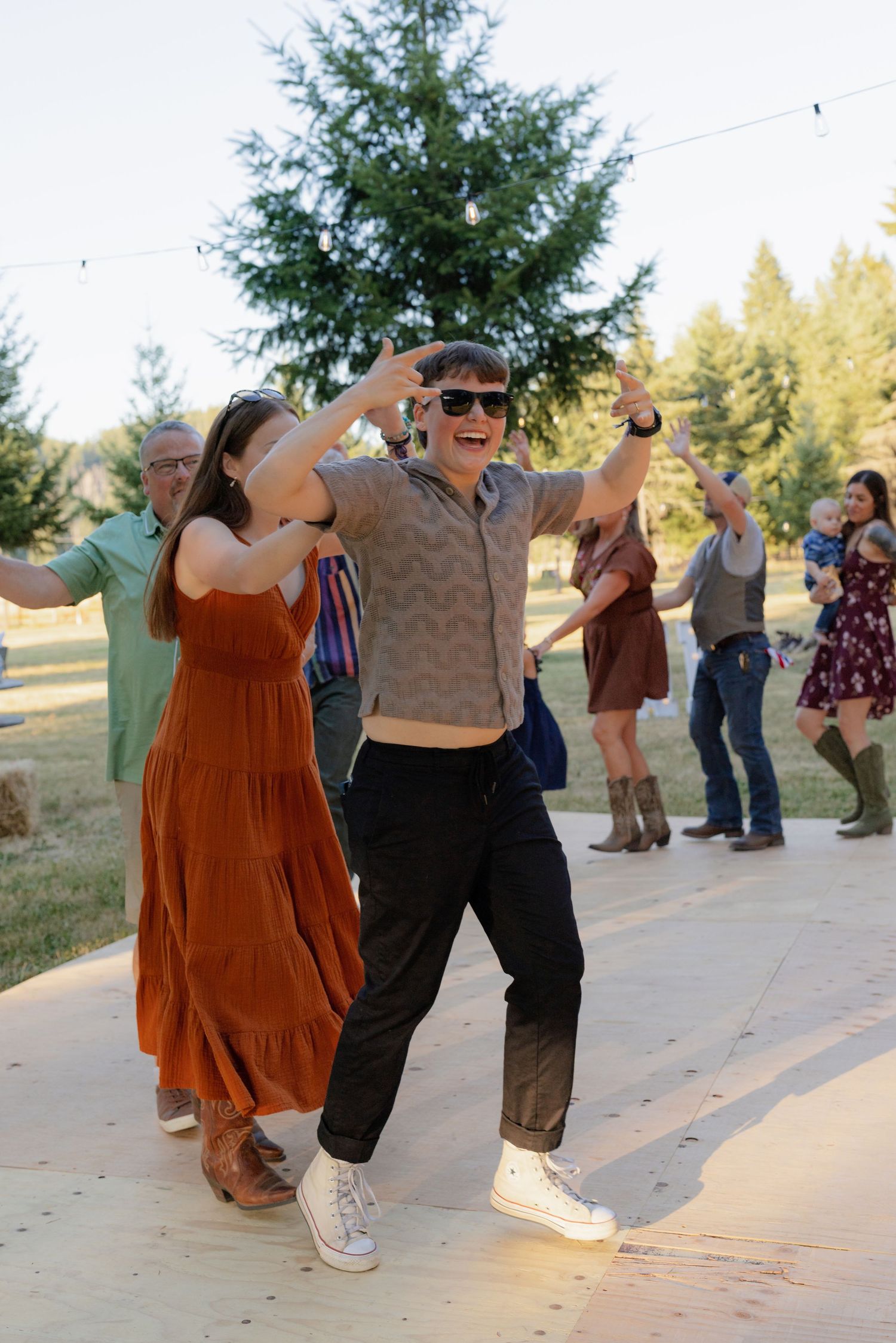 Wedding guests dance joyfully on an outdoor wooden dance floor at a rustic sunset reception.