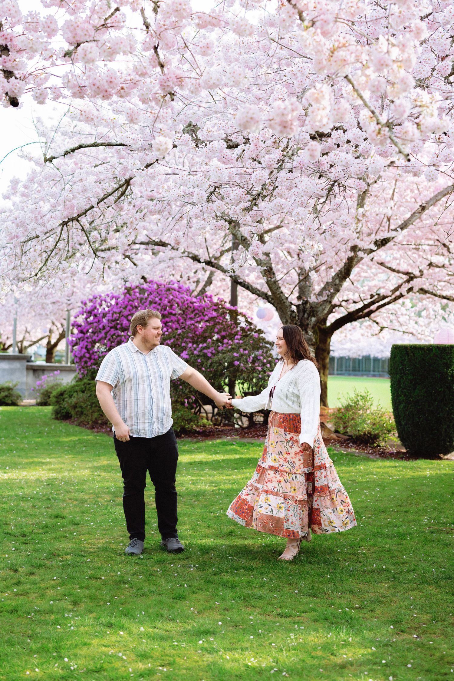 A couple dances together under blooming cherry blossom trees in a spring garden setting.