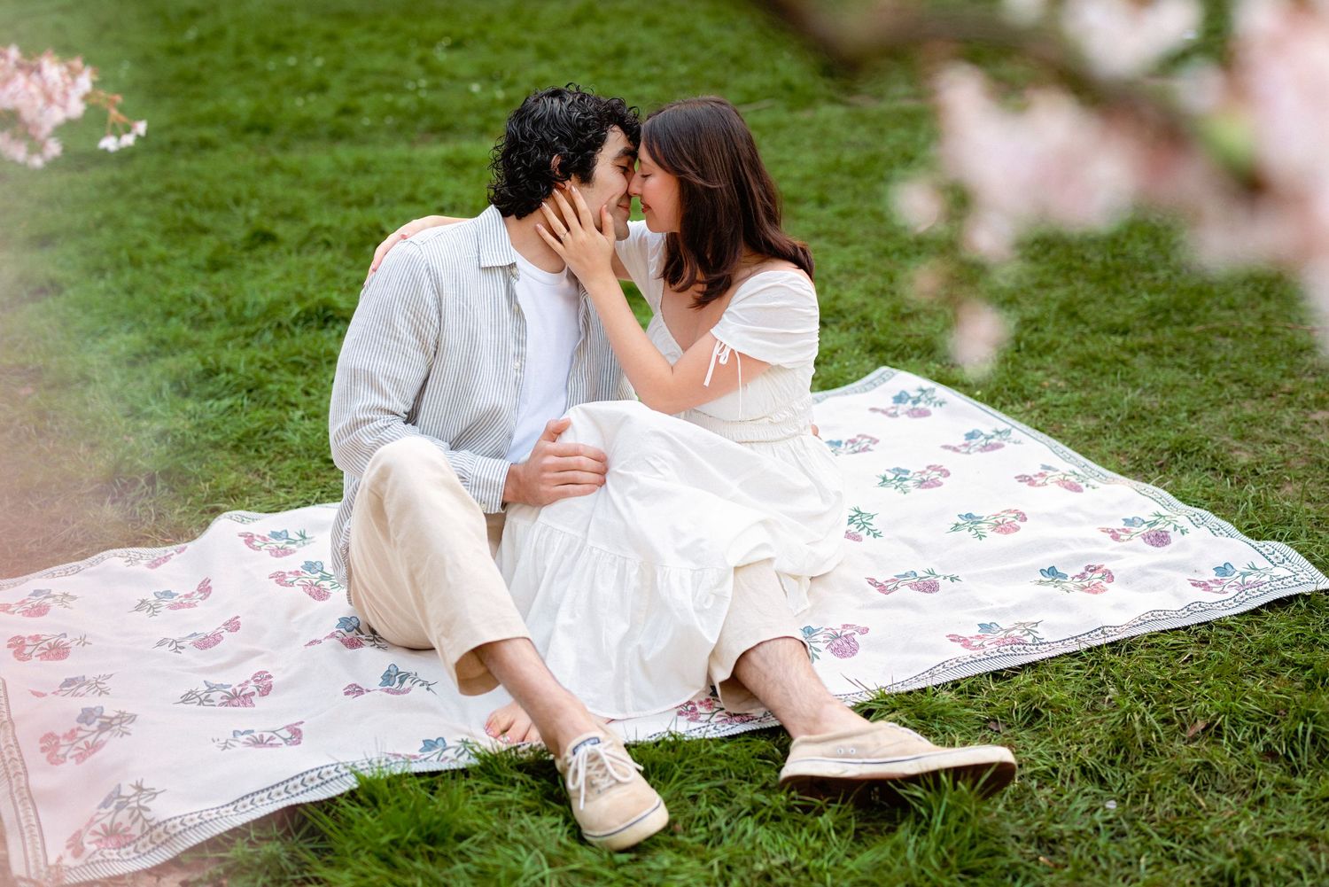 A romantic couple sits on a picnic blanket in a lush green garden during a spring afternoon.