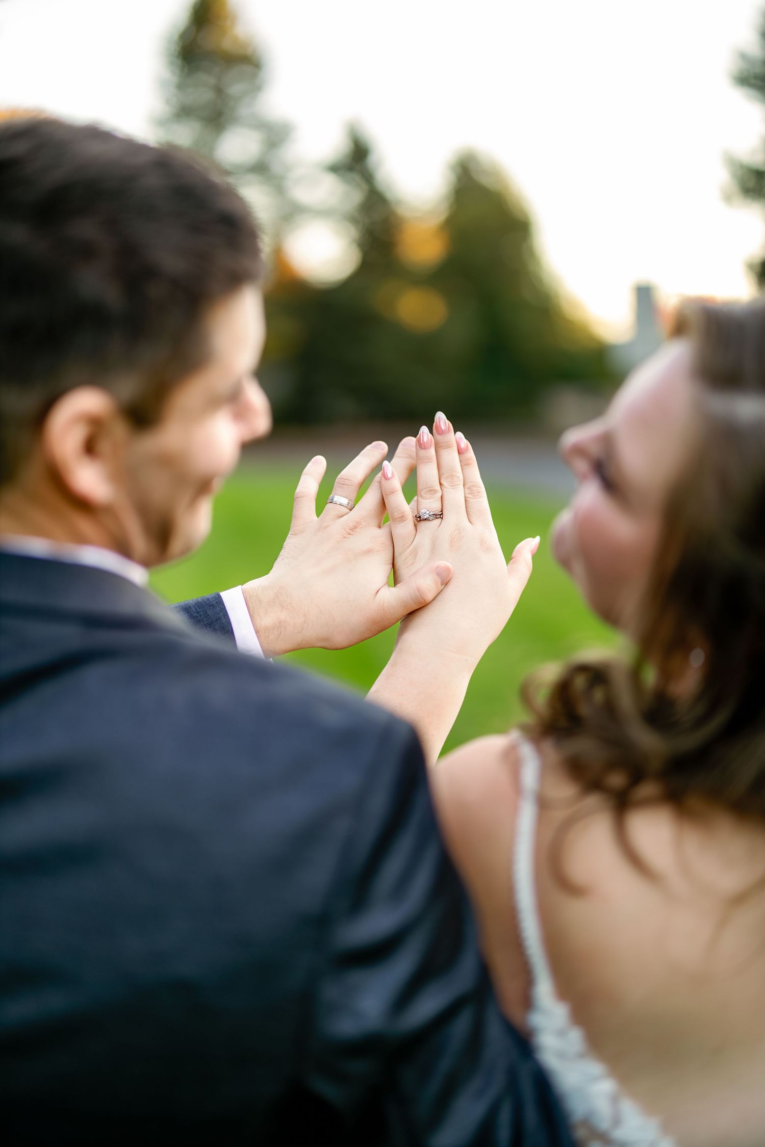 Close-up shot of wedding rings displayed on hands against a sunset background.