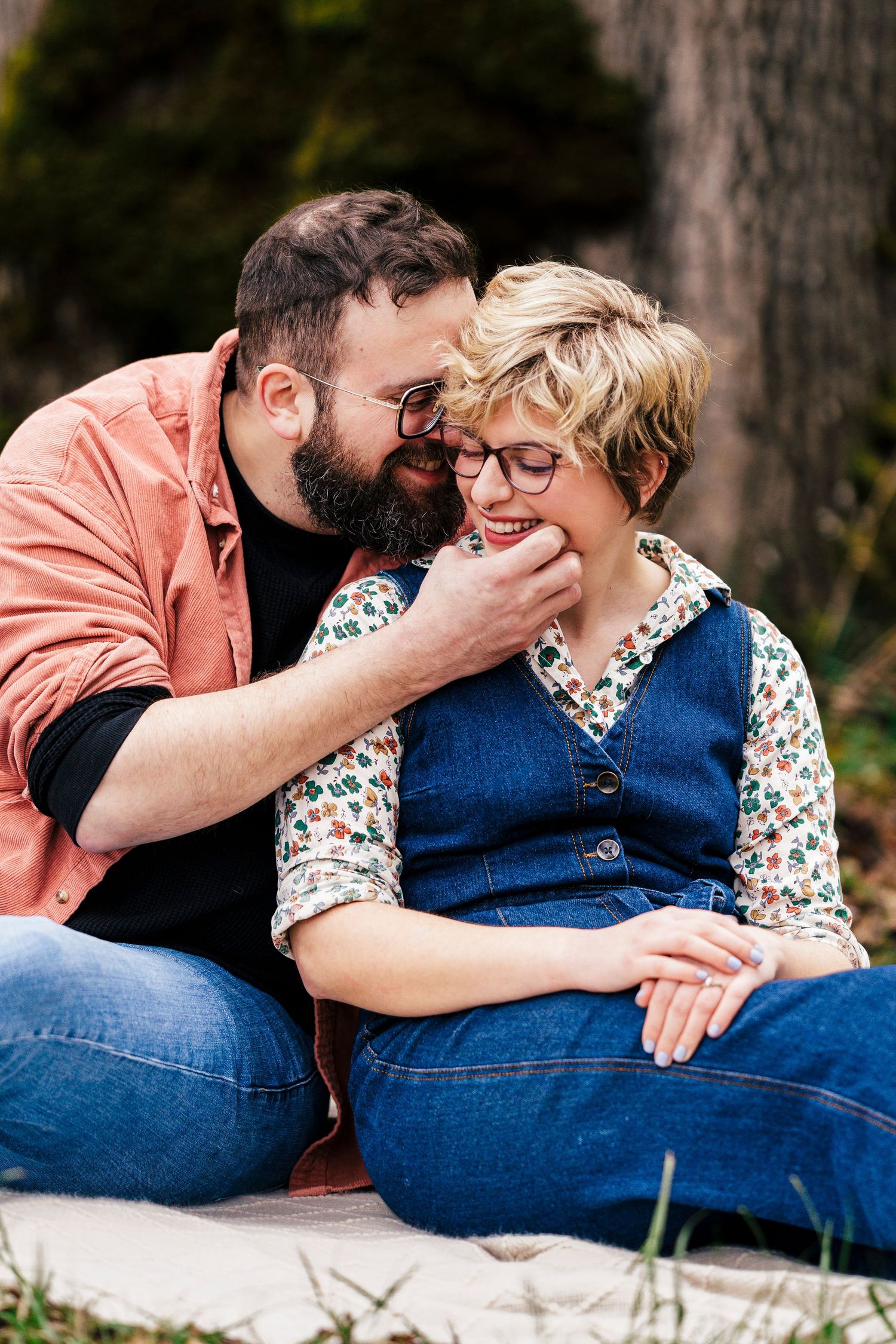 A romantic couple sitting together outdoors, sharing an intimate moment while wearing casual denim and fall attire.