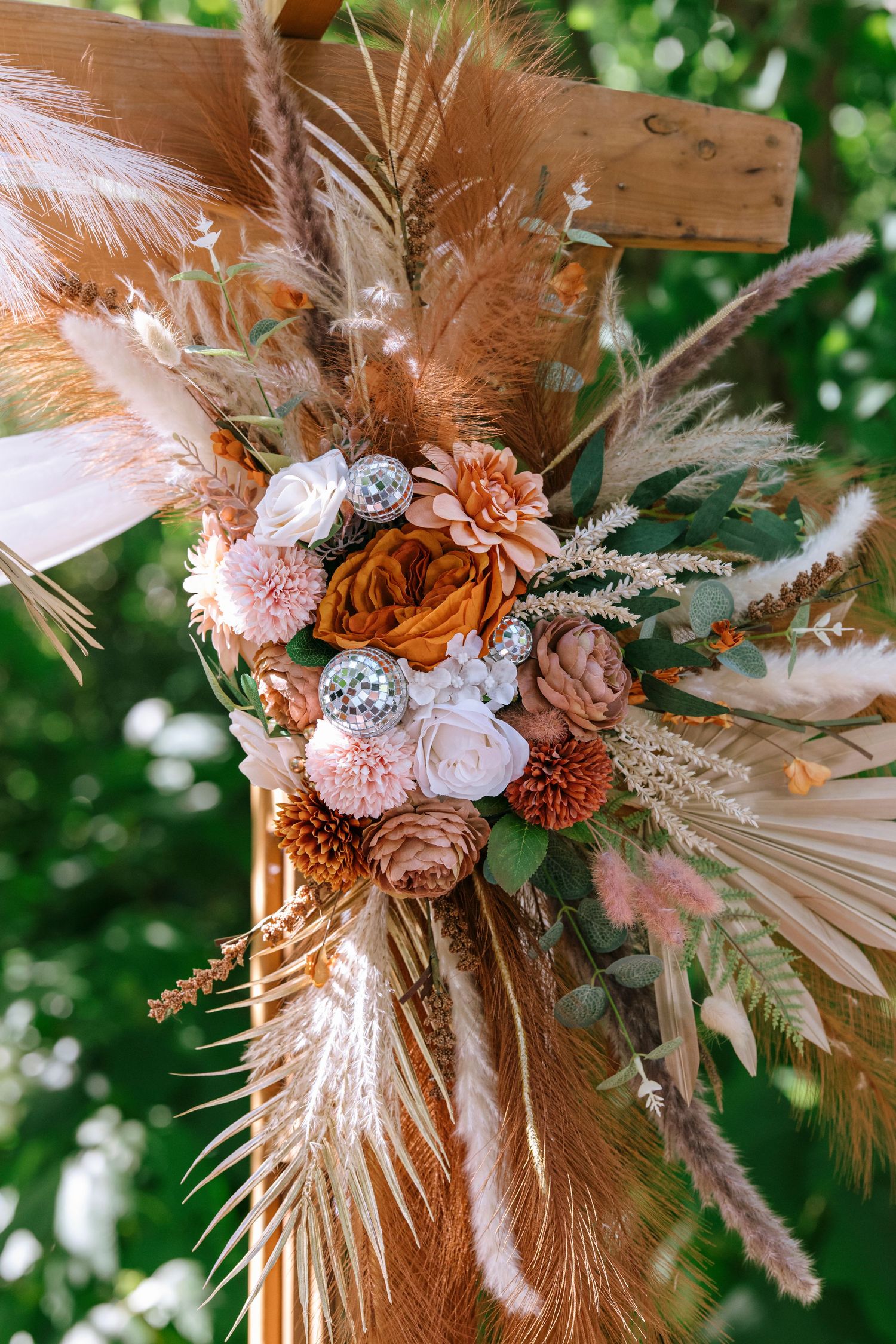Bohemian floral arrangement with dried palm leaves, pink and orange flowers, and pampas grass against a natural backdrop.