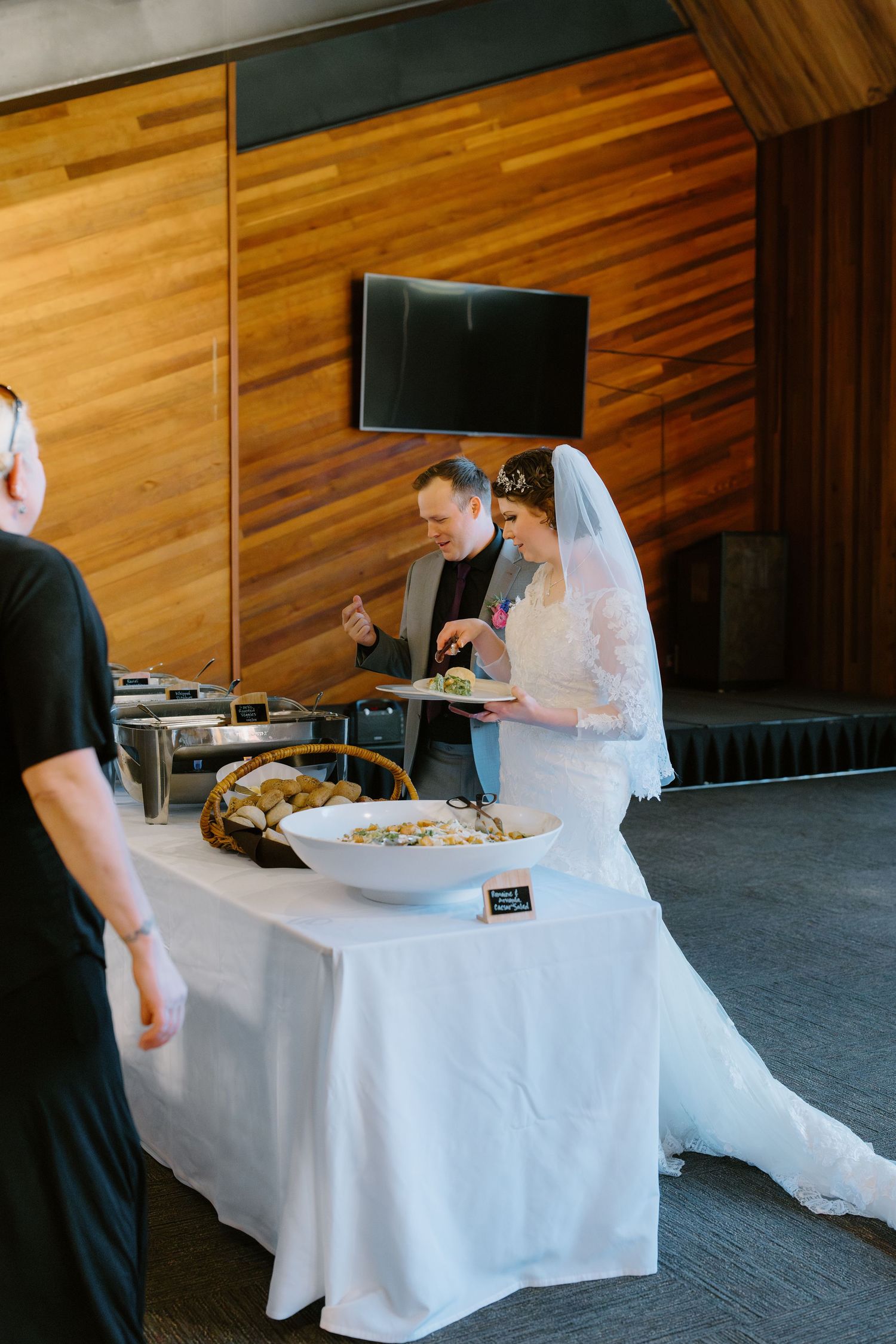 Bride and groom serving themselves at a wedding reception buffet table in an elegant modern venue.