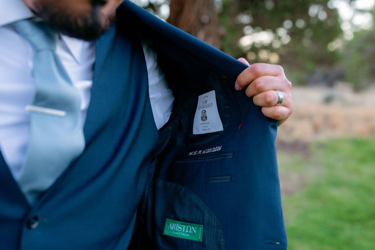Close-up of Austin brand label inside navy blue groom's suit jacket at outdoor wedding.