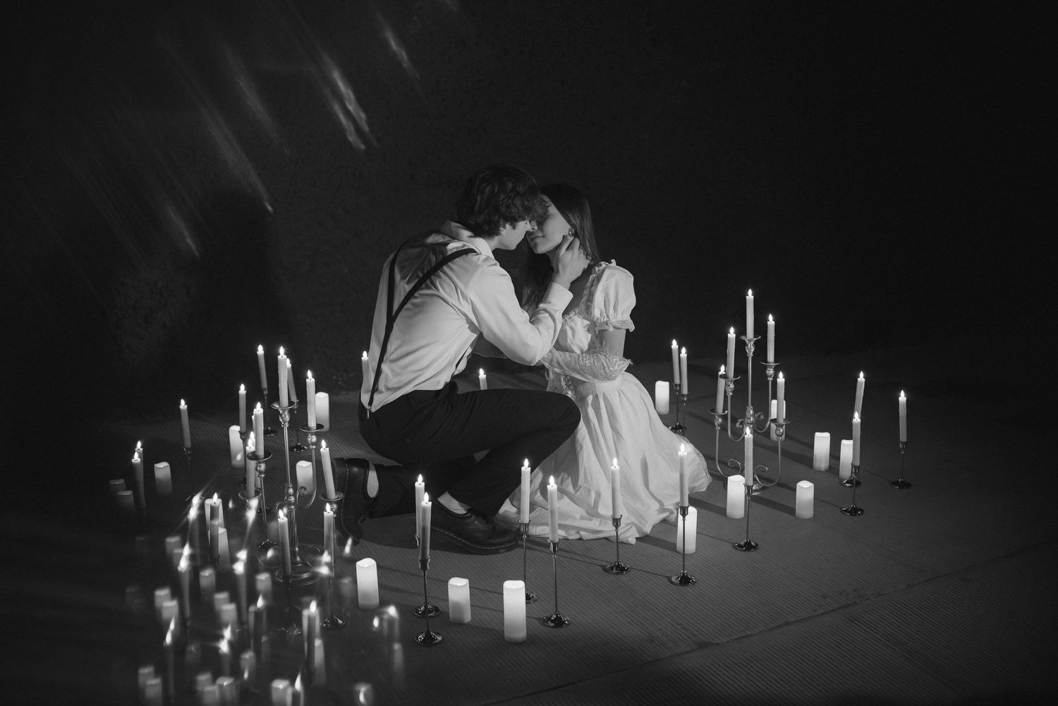 A row of lit white candles glowing in the darkness during a memorial or vigil service.