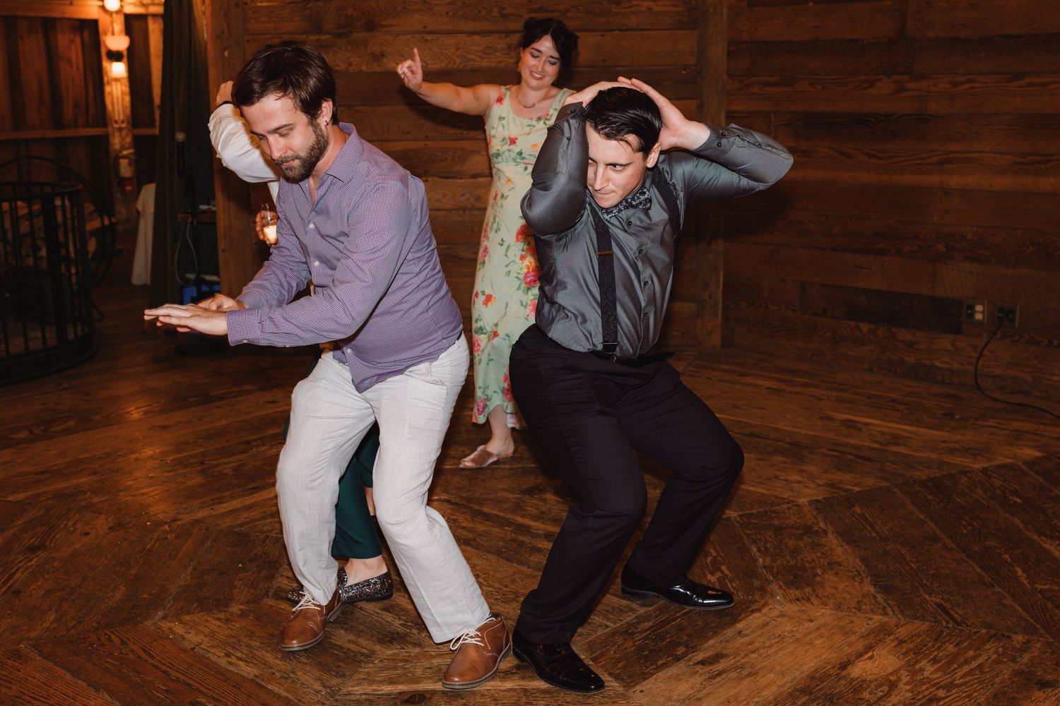 Two men energetically dance together on a wooden dance floor at a lively indoor wedding reception.