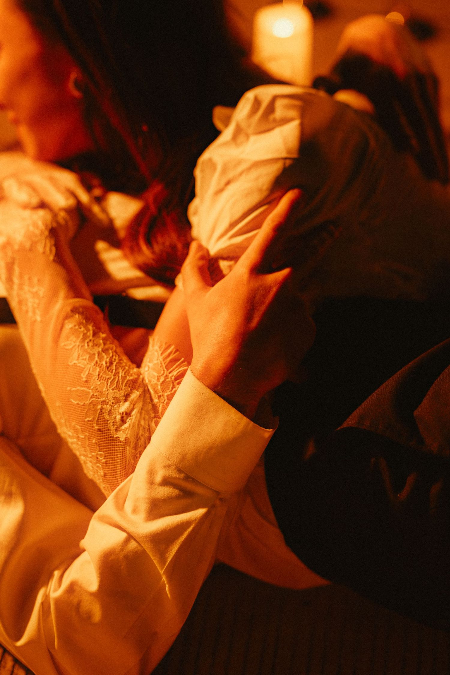 Close-up detail of lace sleeves and hands in warm candlelight creating a romantic atmosphere.