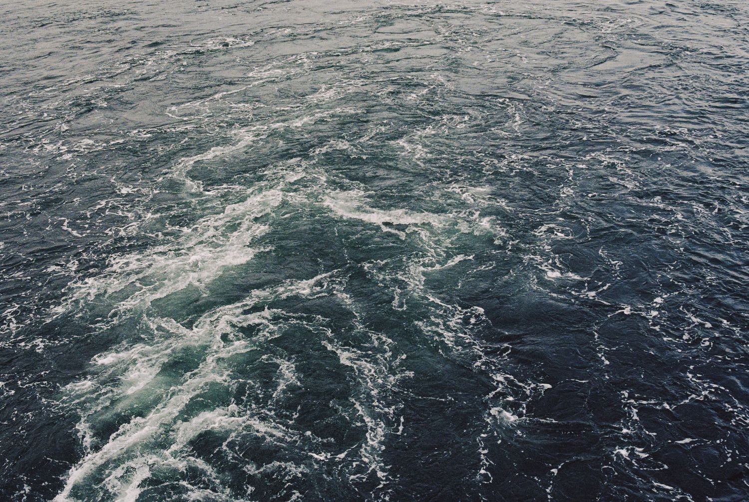 Turbulent dark blue ocean water with white foam swirls and waves on the open sea.