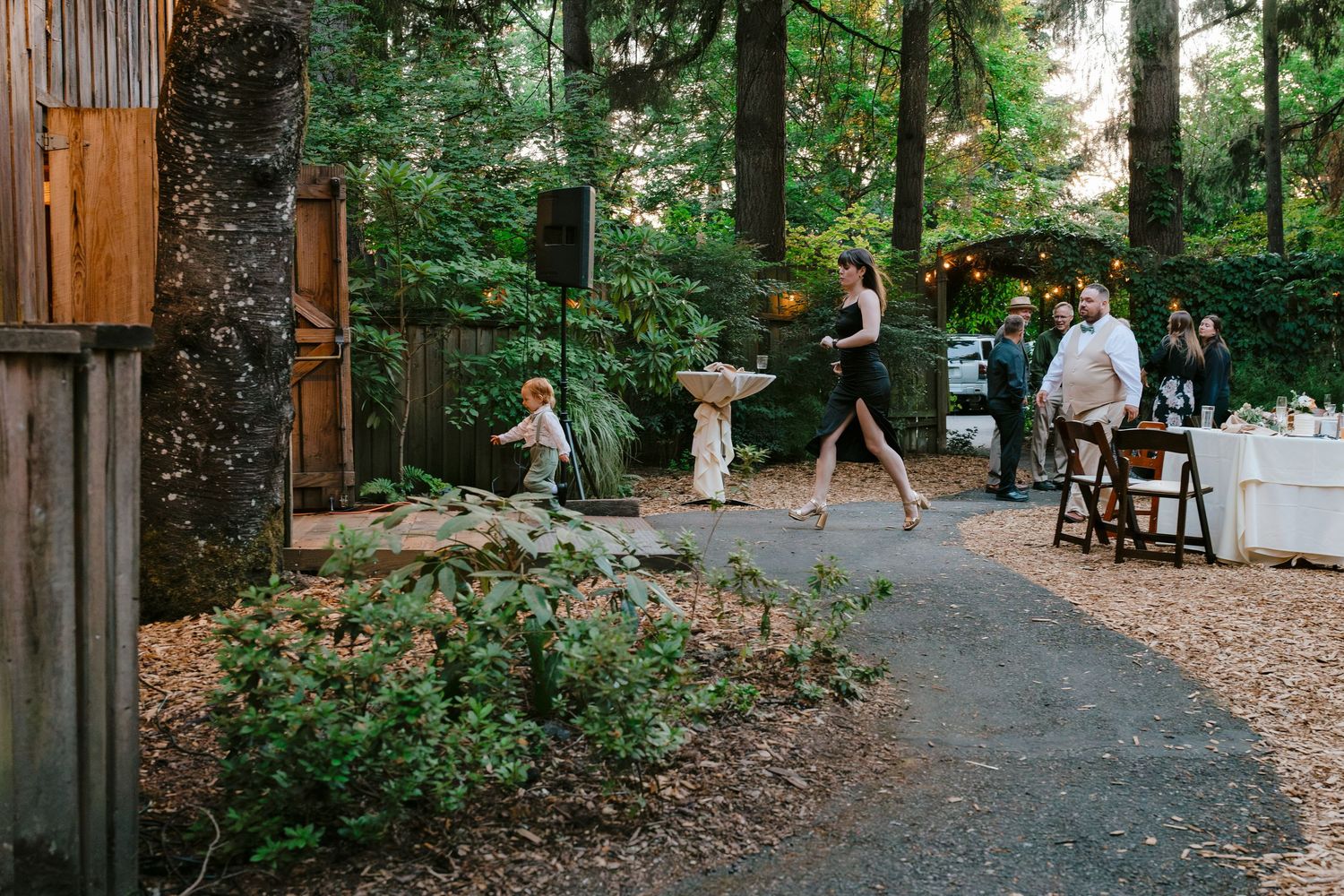 Guests walking along a wooded garden path at an outdoor wedding venue surrounded by trees.