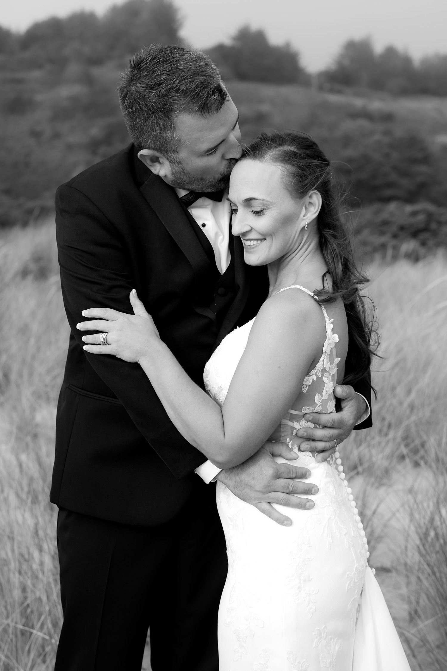 Black and white portrait of a loving embrace against a natural outdoor backdrop.