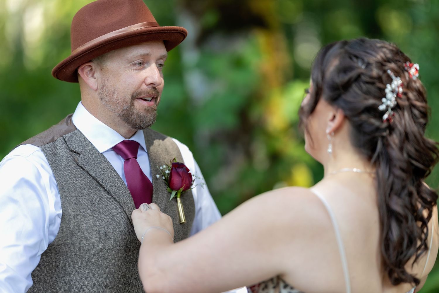 Wedding party in vintage-inspired attire with brown hats and vests posing outdoors in natural lighting.