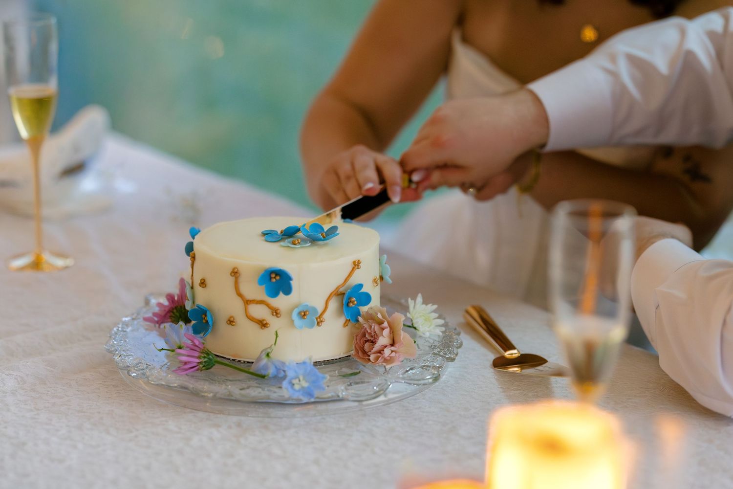 Close-up shots of hands decorating a white wedding cake with delicate blue floral details.