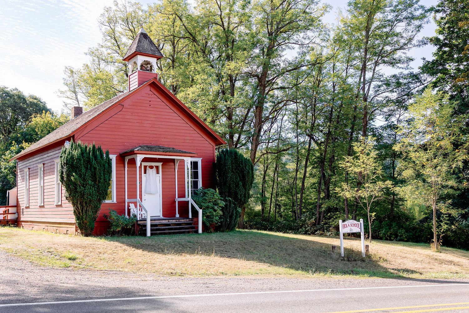 Panoramic view of a red wooden church or community building nestled among trees in a rural setting.