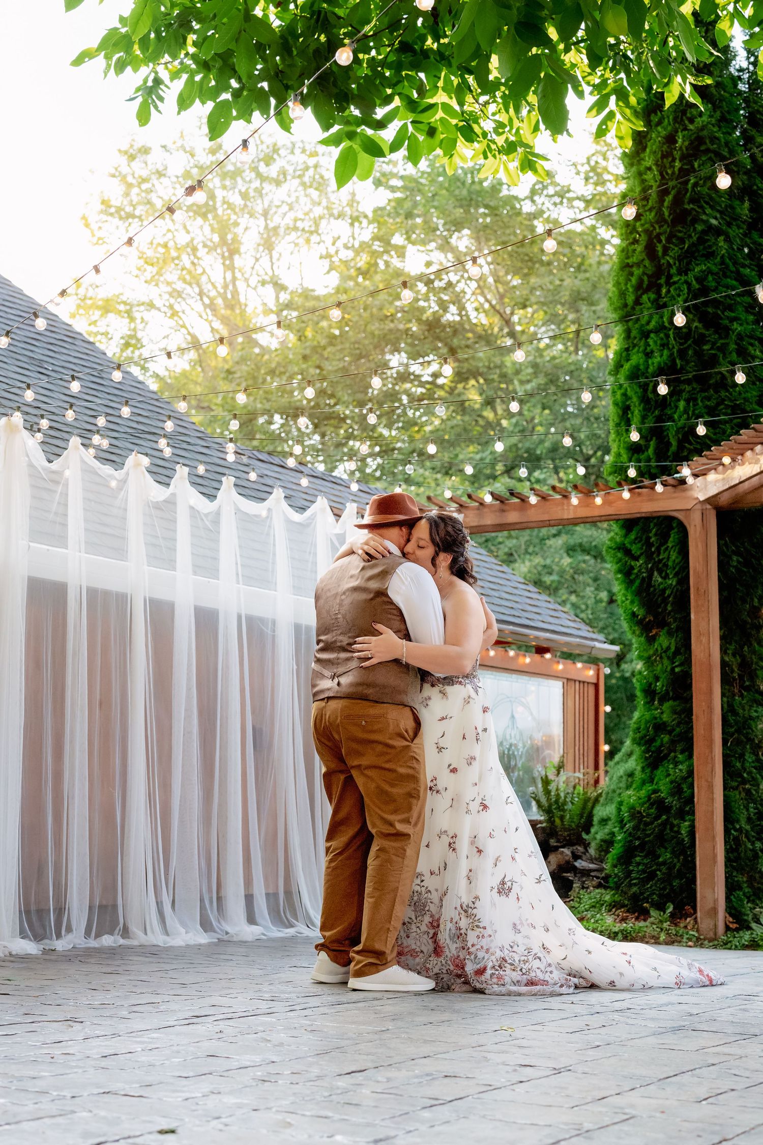 A couple shares an intimate moment on an outdoor patio decorated with white drapes and string lights.
