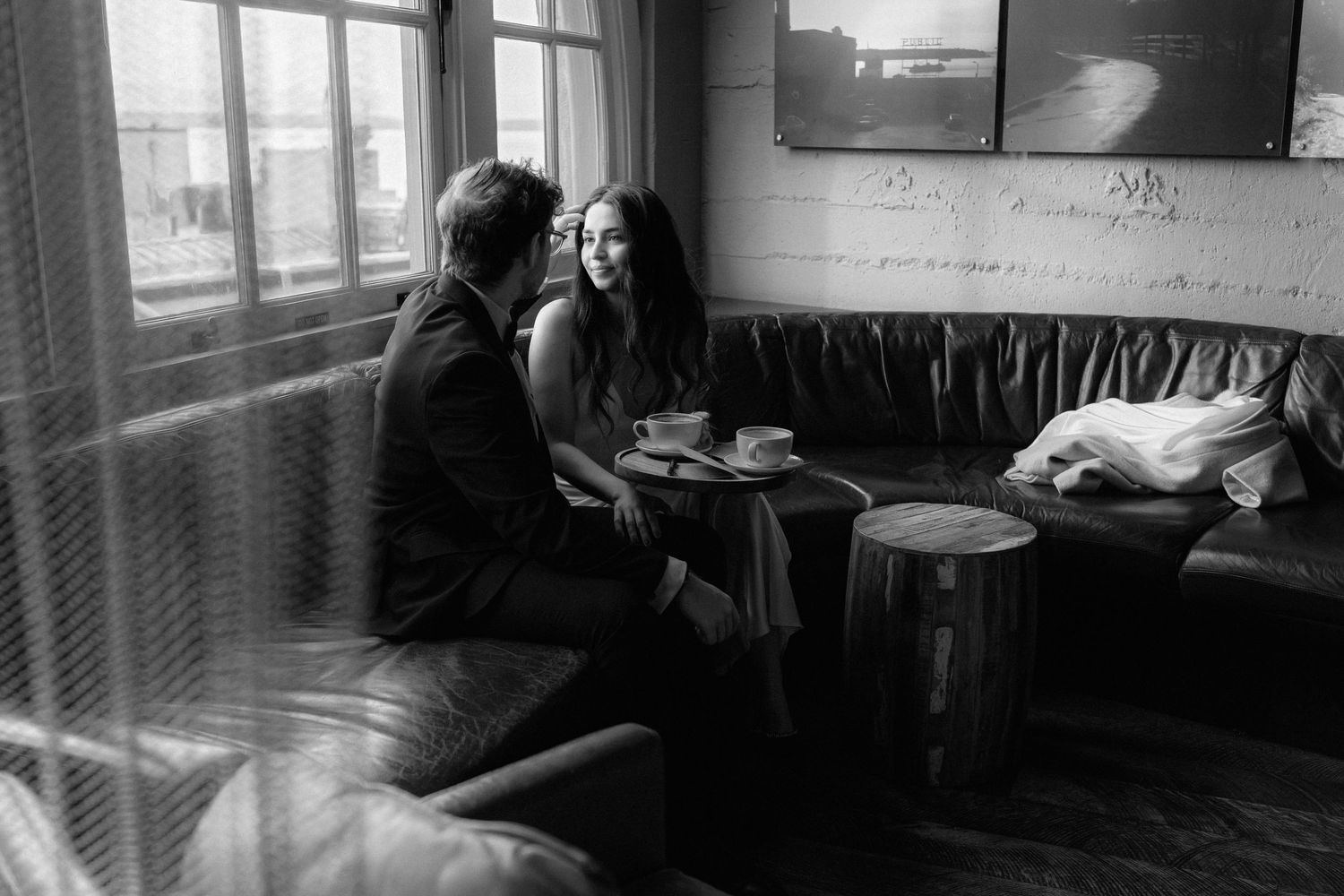 Black and white photograph of people seated in a dimly lit cafe interior with windows and tables.