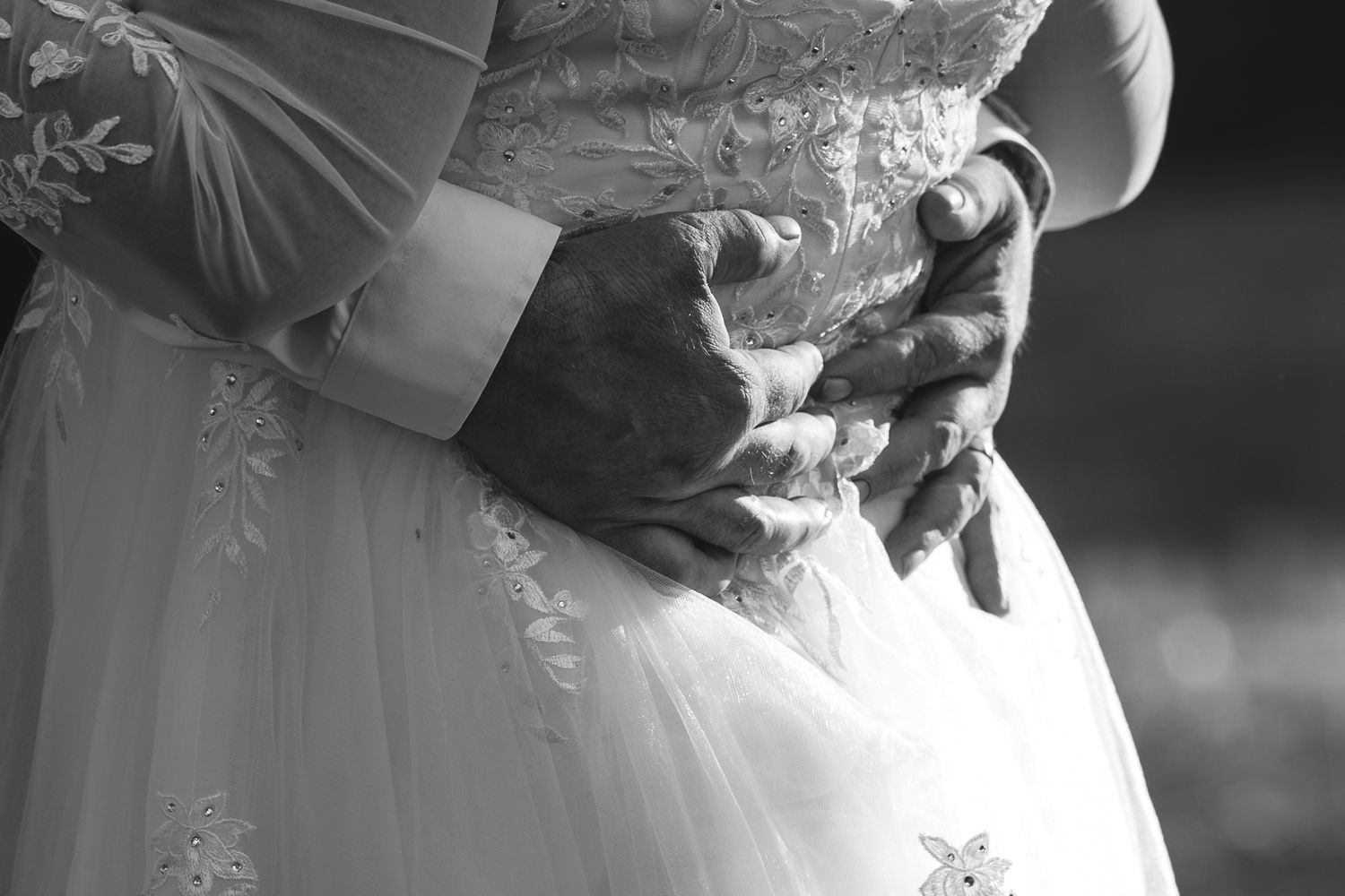 Black and white wedding photograph showing a couple in formal attire embracing during an intimate moment.
