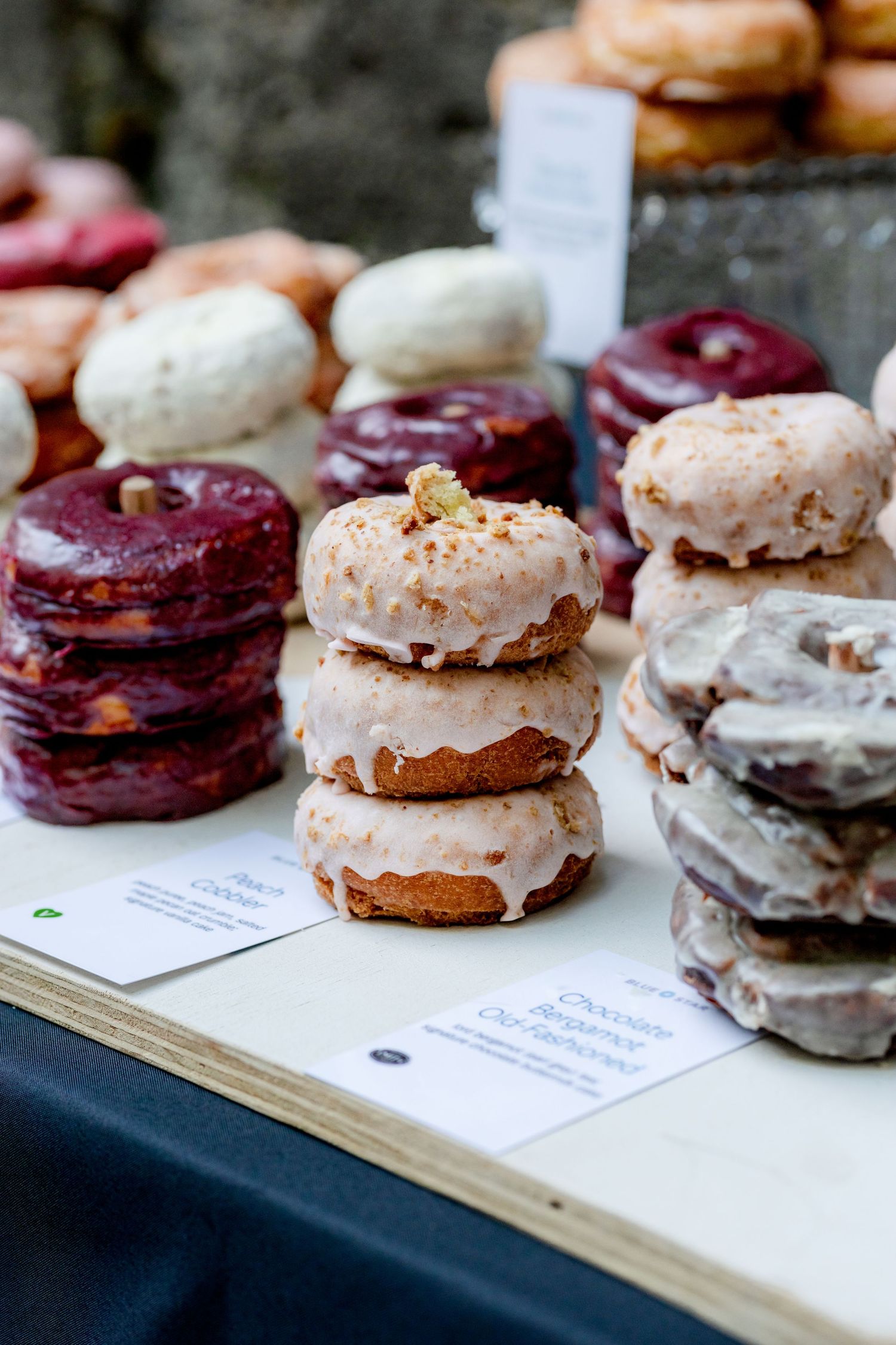 Stacks of assorted frosted donuts displayed on a wooden table with flavor labels at a wedding dessert station.