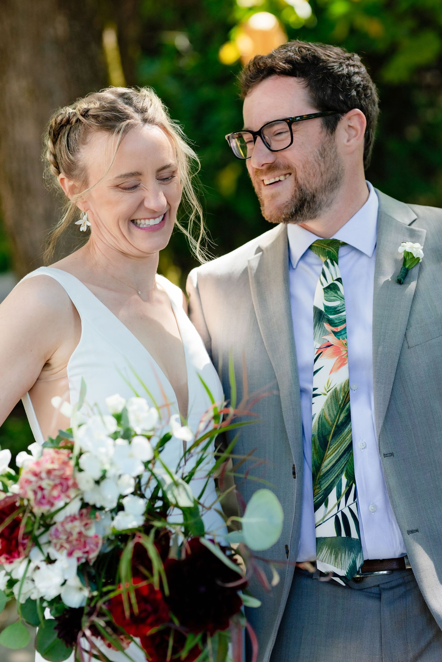 Smiling bride and groom in gray suit with tropical tie share a joyful moment outdoors on their wedding day.