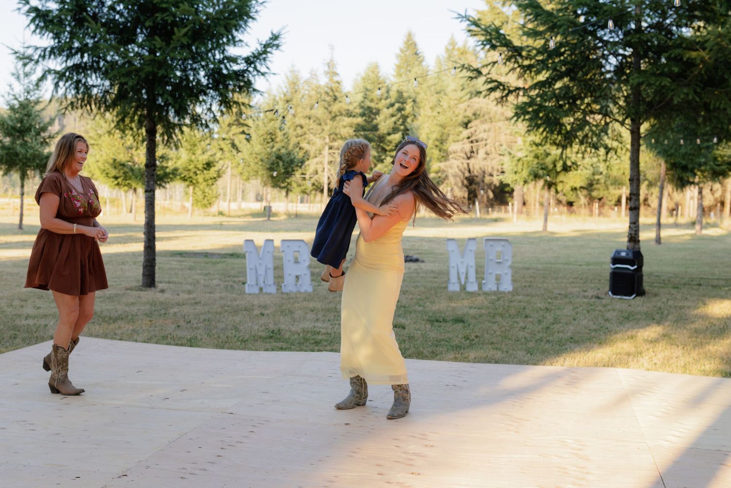 Woman in yellow dress lifting a child while another woman watches near Mr and Mr signs.