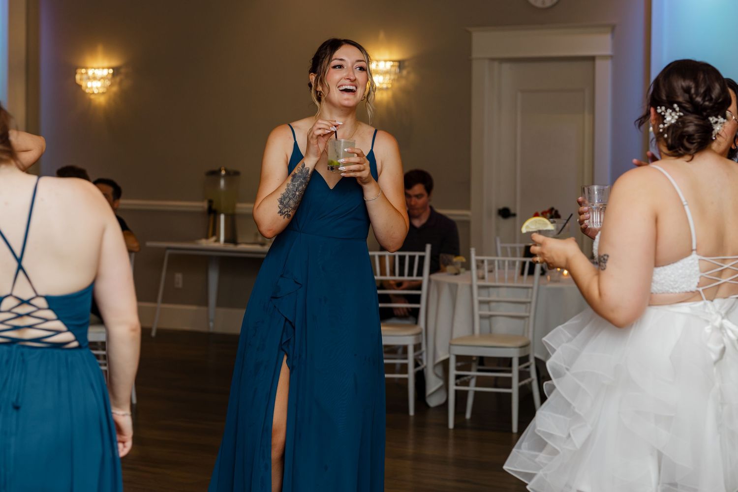 Bridesmaid in teal gown smiles and dances with champagne at wedding reception.