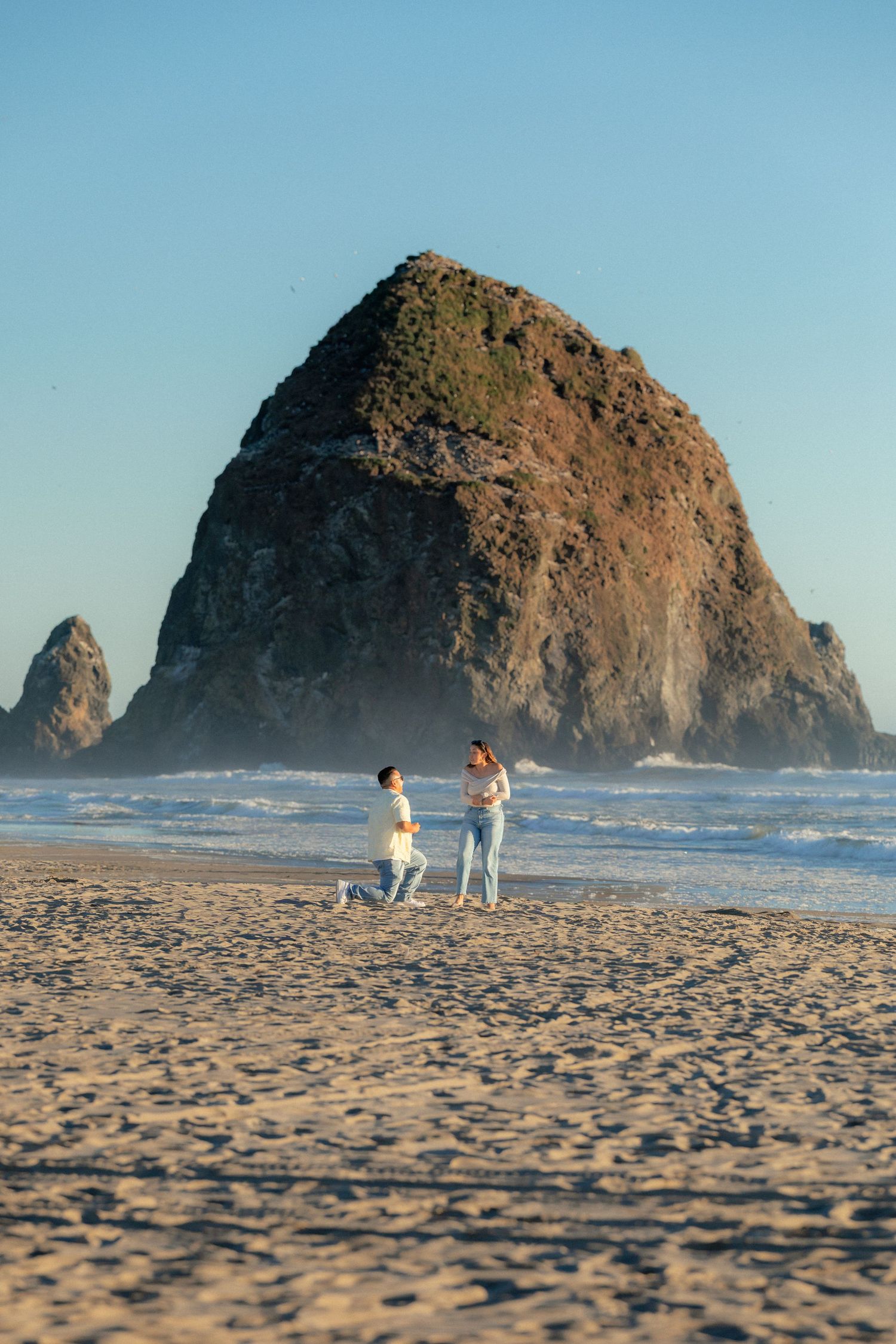 Two people strolling along sandy Cannon Beach with massive Haystack Rock rising from the ocean.