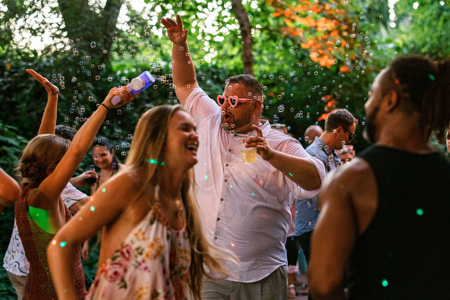 Group of friends dancing outdoors at a garden party with confetti and bubbles filling the air.