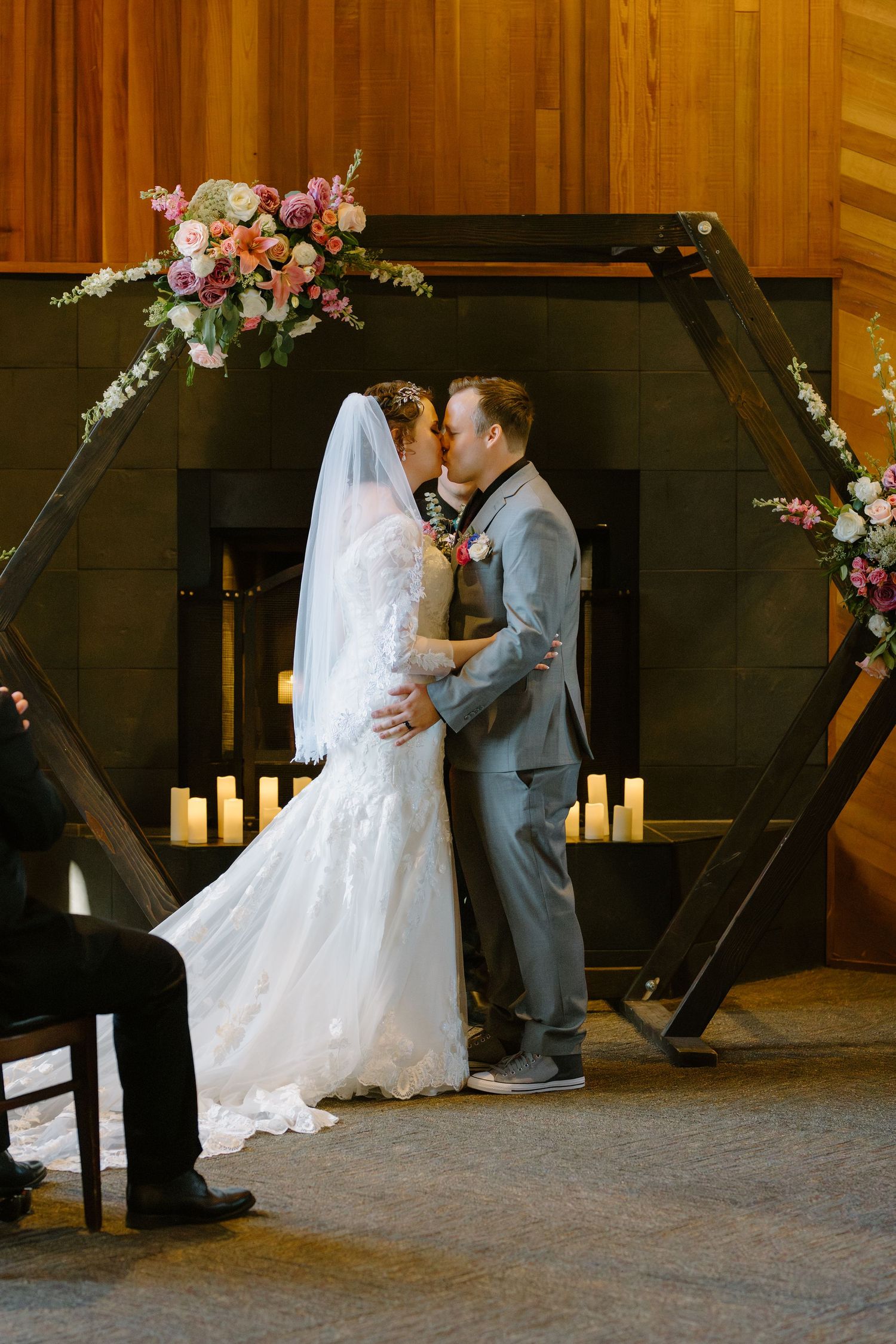 Bride and groom share first kiss under a hexagonal floral arch with candles at wedding ceremony.