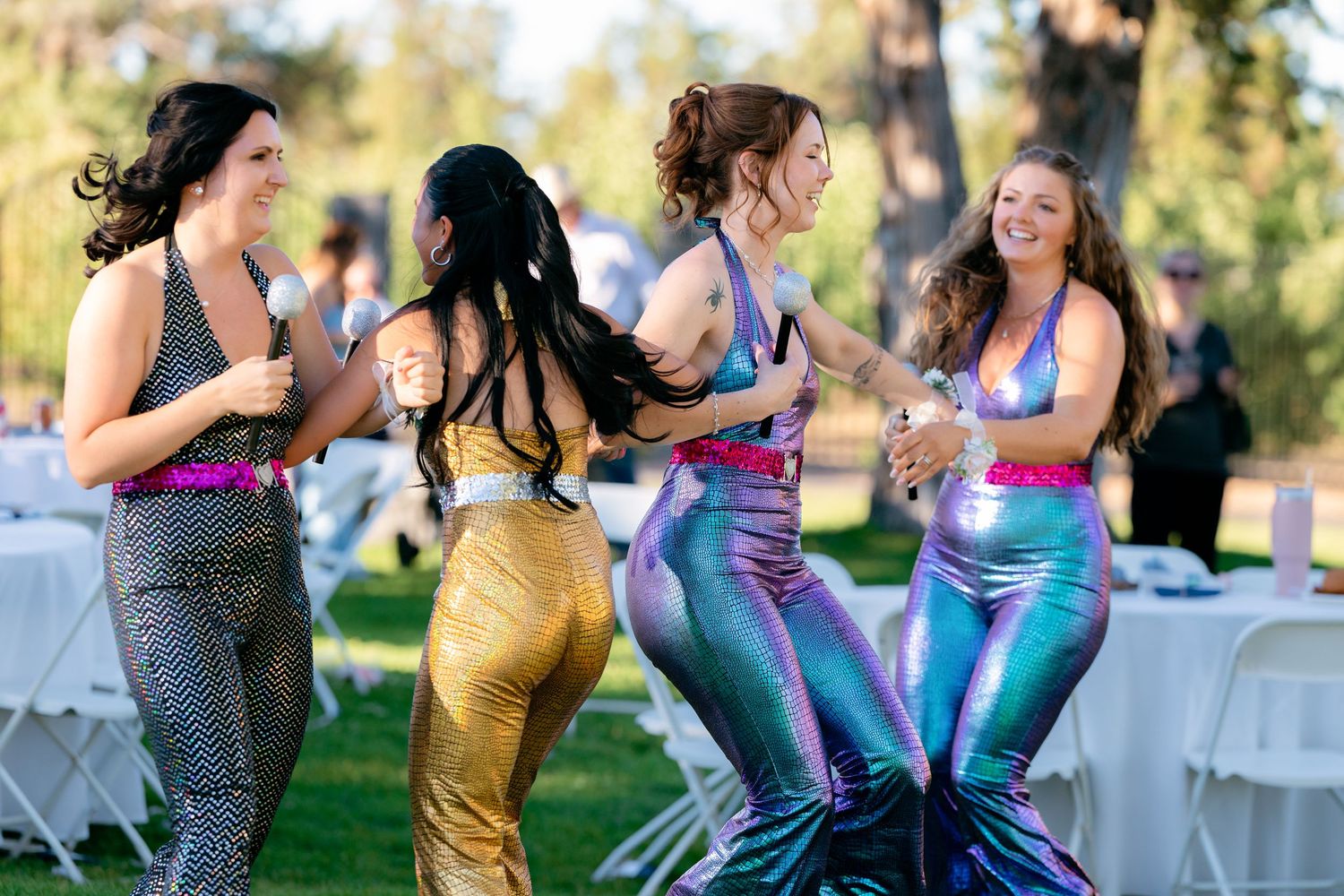 Four women in colorful mermaid costumes dance and celebrate together at outdoor wedding reception.