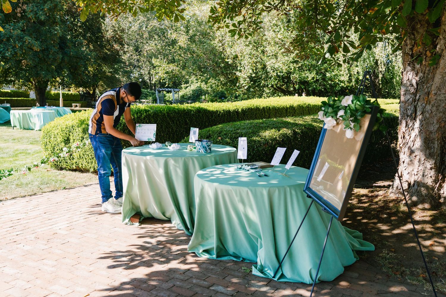 Outdoor reception setup with turquoise tablecloths under shaded trees.