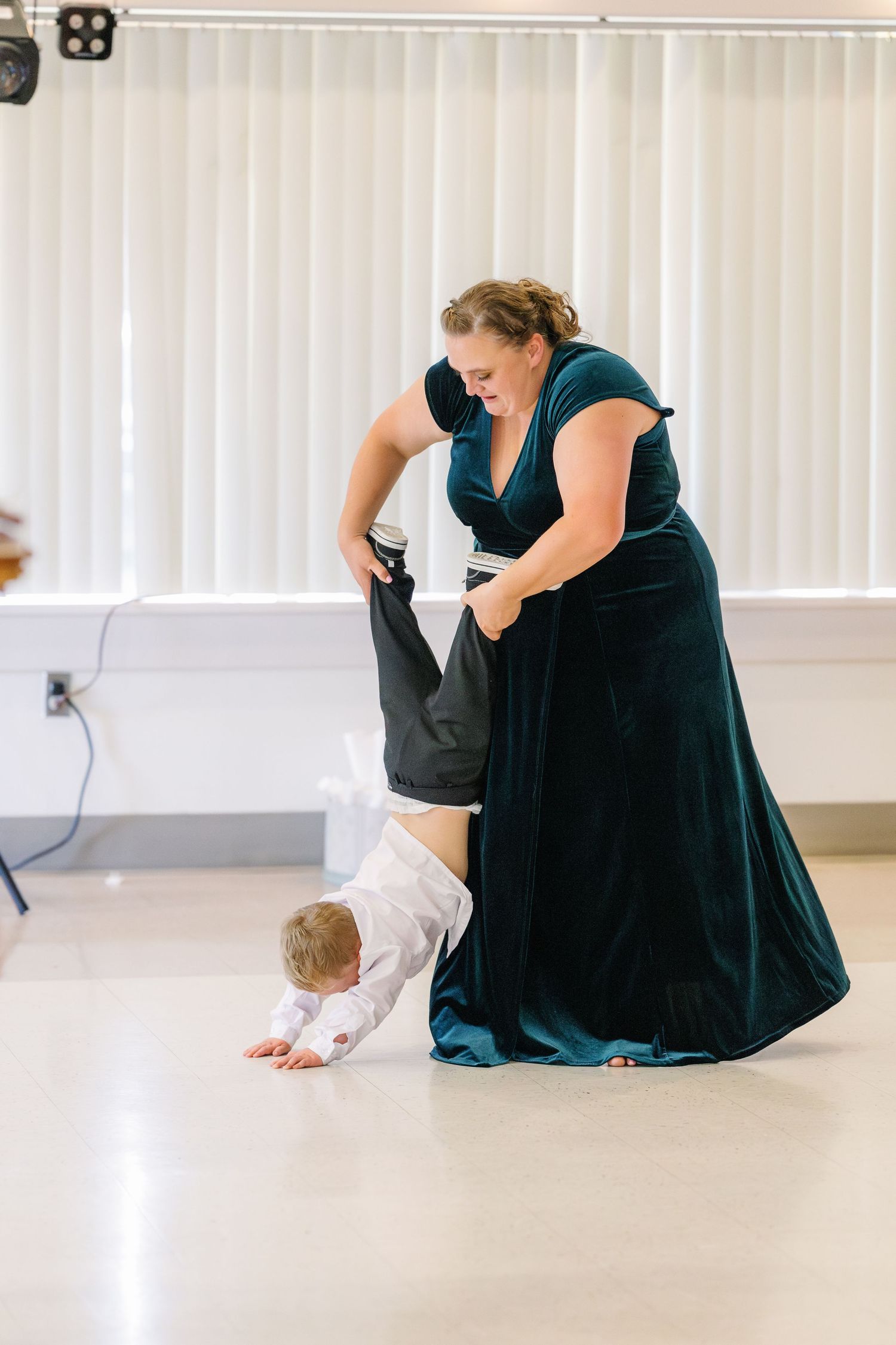 A person in a dark dress sits on a light colored floor in a dance or performance space.