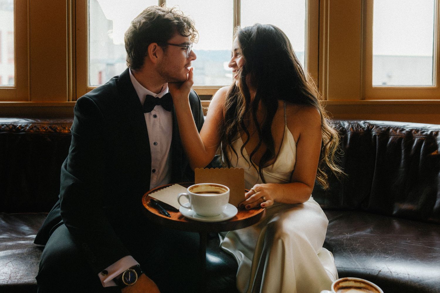 Intimate wedding couple moment on vintage leather couch in warm indoor lighting.