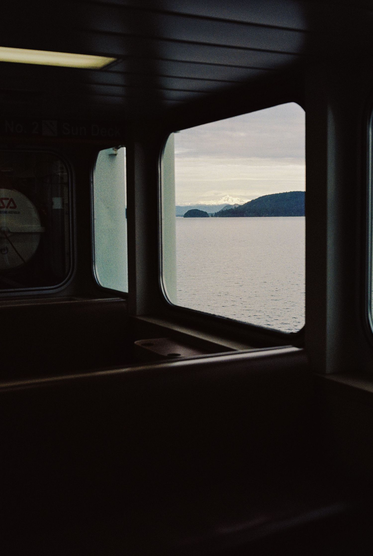 Serene ocean view with distant mountains framed through dark ferry window at dusk.